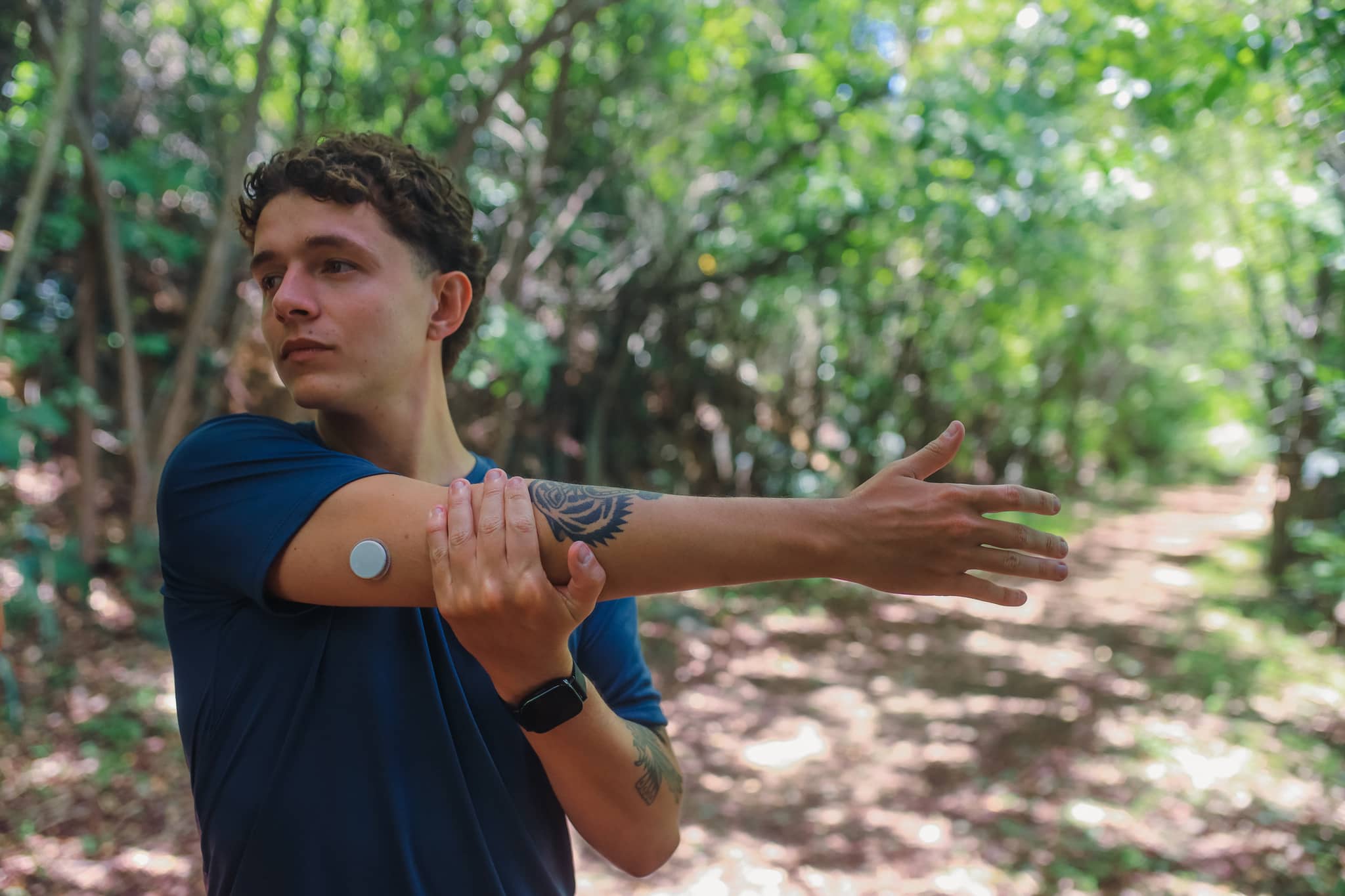 Ein junger Mann mit Diabetes-Sensor am Arm dehnt sich.
