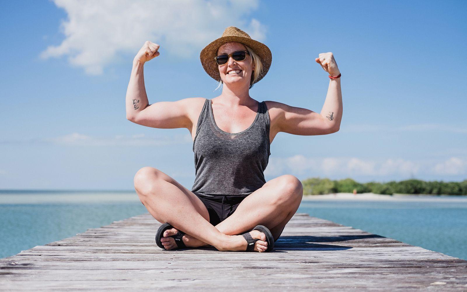 Mind-Muscle-Connection: Glückliche Frau, die ihre Armmuskeln anspannt