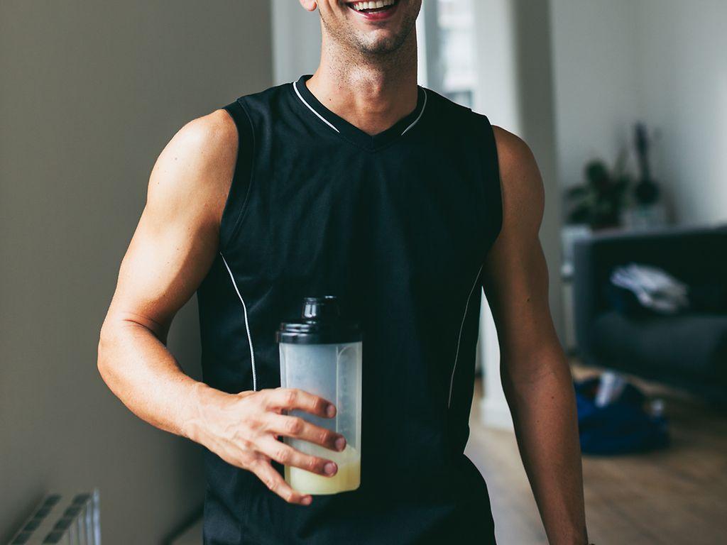 Lächelnder Mann, der einen Proteinshake nach hartem Training trinkt
