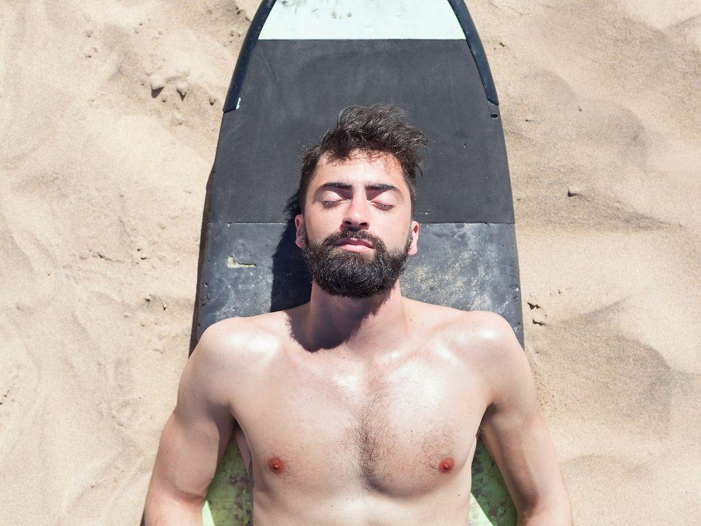 Hübscher Surfer entspannt sich am Strand