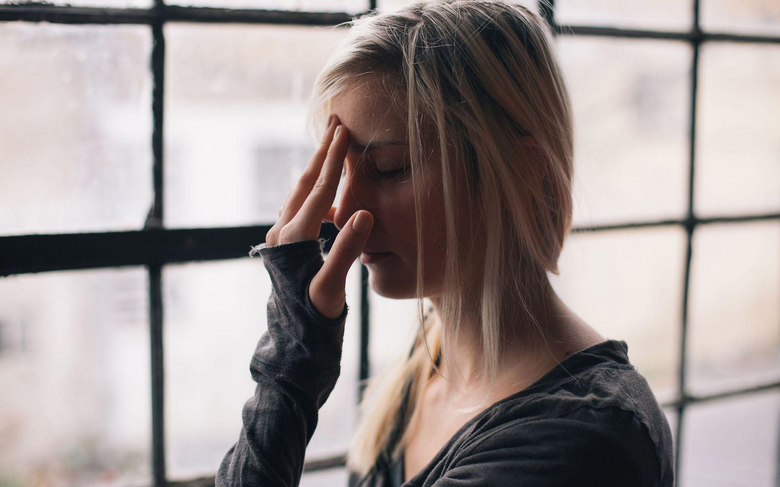Schimmelpilzallergie: Frau mit geschlossenen Augen fässt sich mit einer Hand an die Stirn.