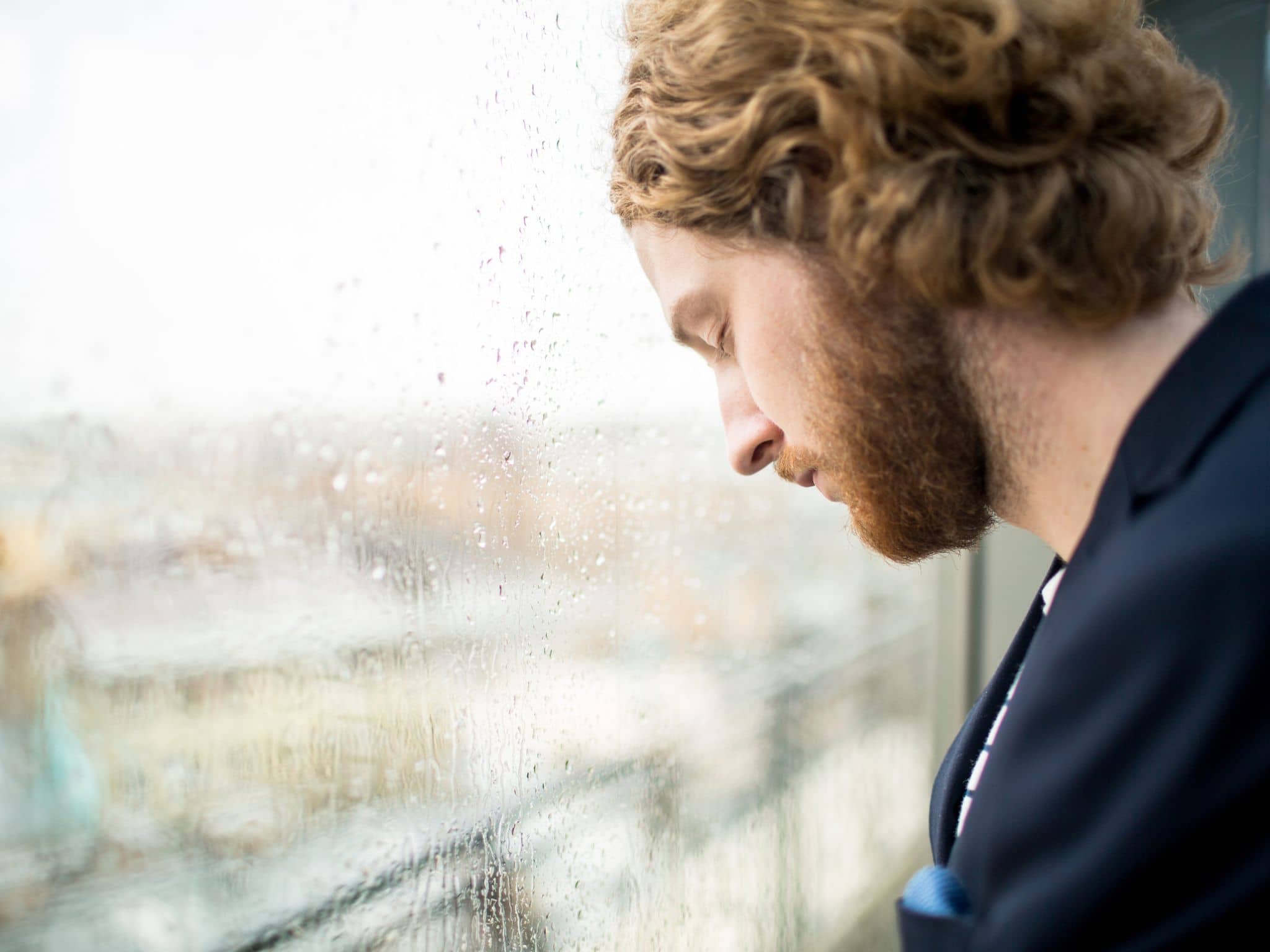 Bild: Trauriger Mann steht bei Regenwetter mit geschlossenen Augen am Fenster.