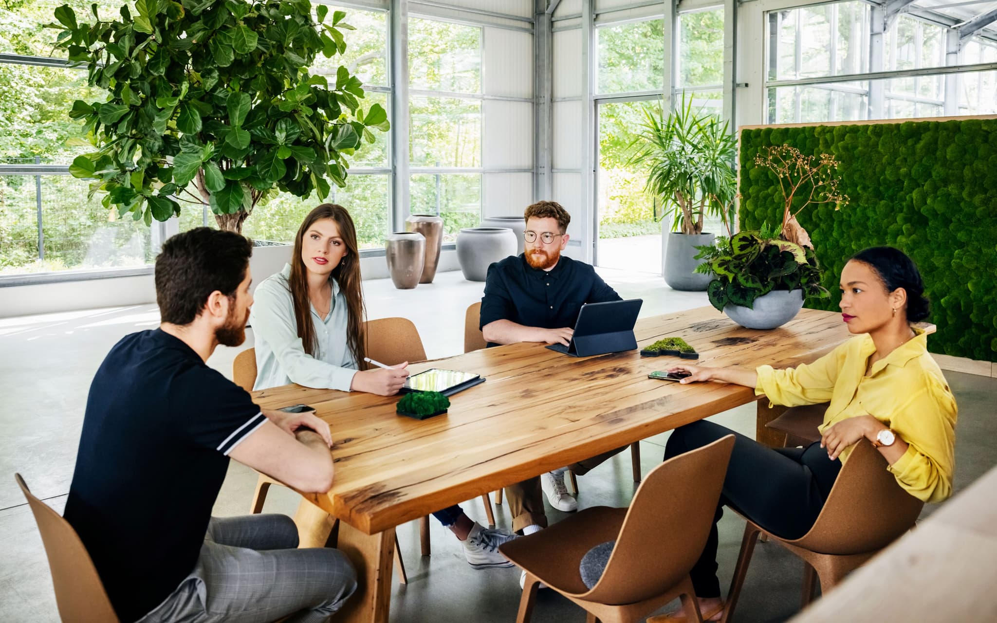 Nachhaltigkeit im Arbeitsalltag: Eine Gruppe von Kolleginnen und Kollegen sitzt in einem begrünten Büro