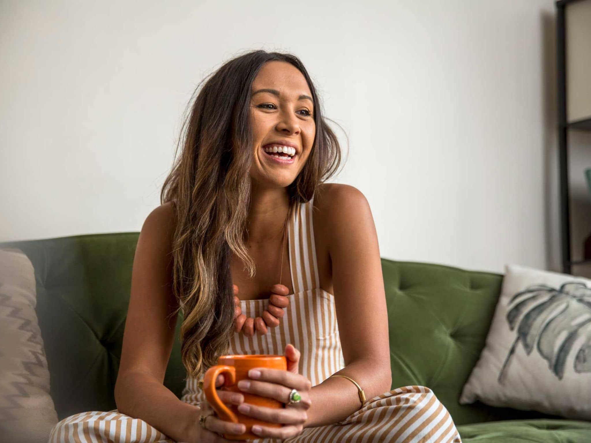 Junge Frau lacht fröhlich und hält eine Tasse in den Händen