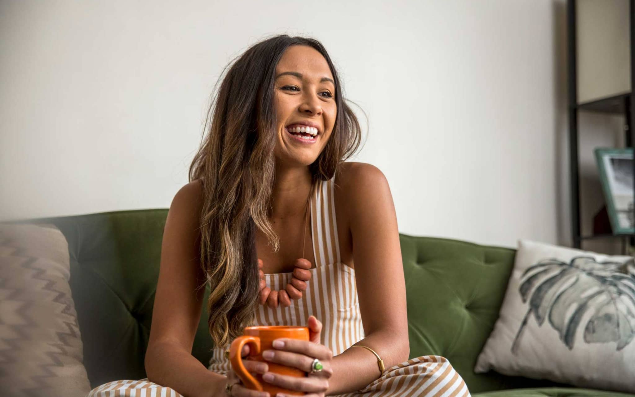 Junge Frau lacht fröhlich und hält eine Tasse in den Händen