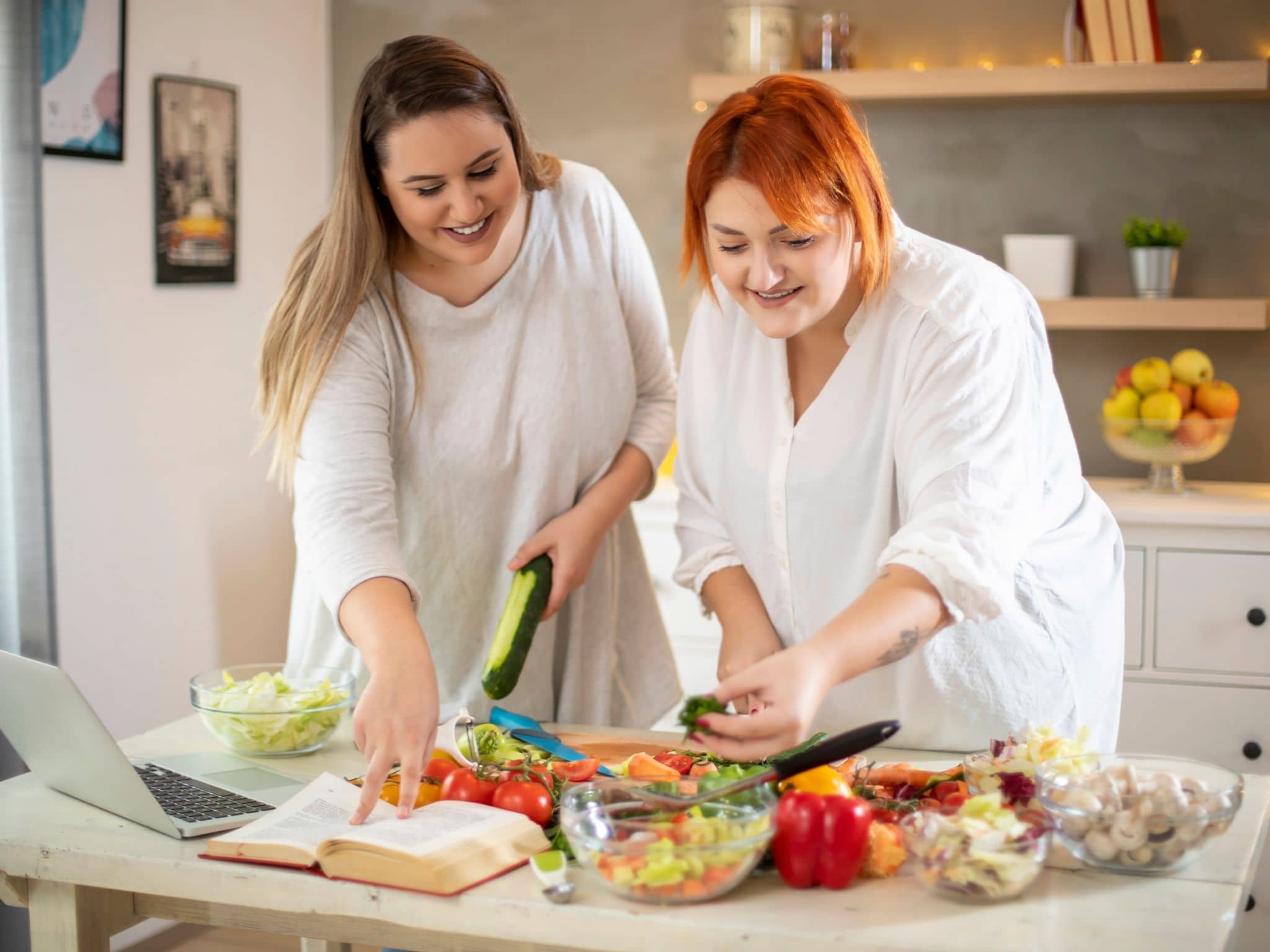 Abnehmtipps vom Ernährungsmediziner: Zwei Frauen mit Übergewicht kochen gesundes Essen nach Anleitung