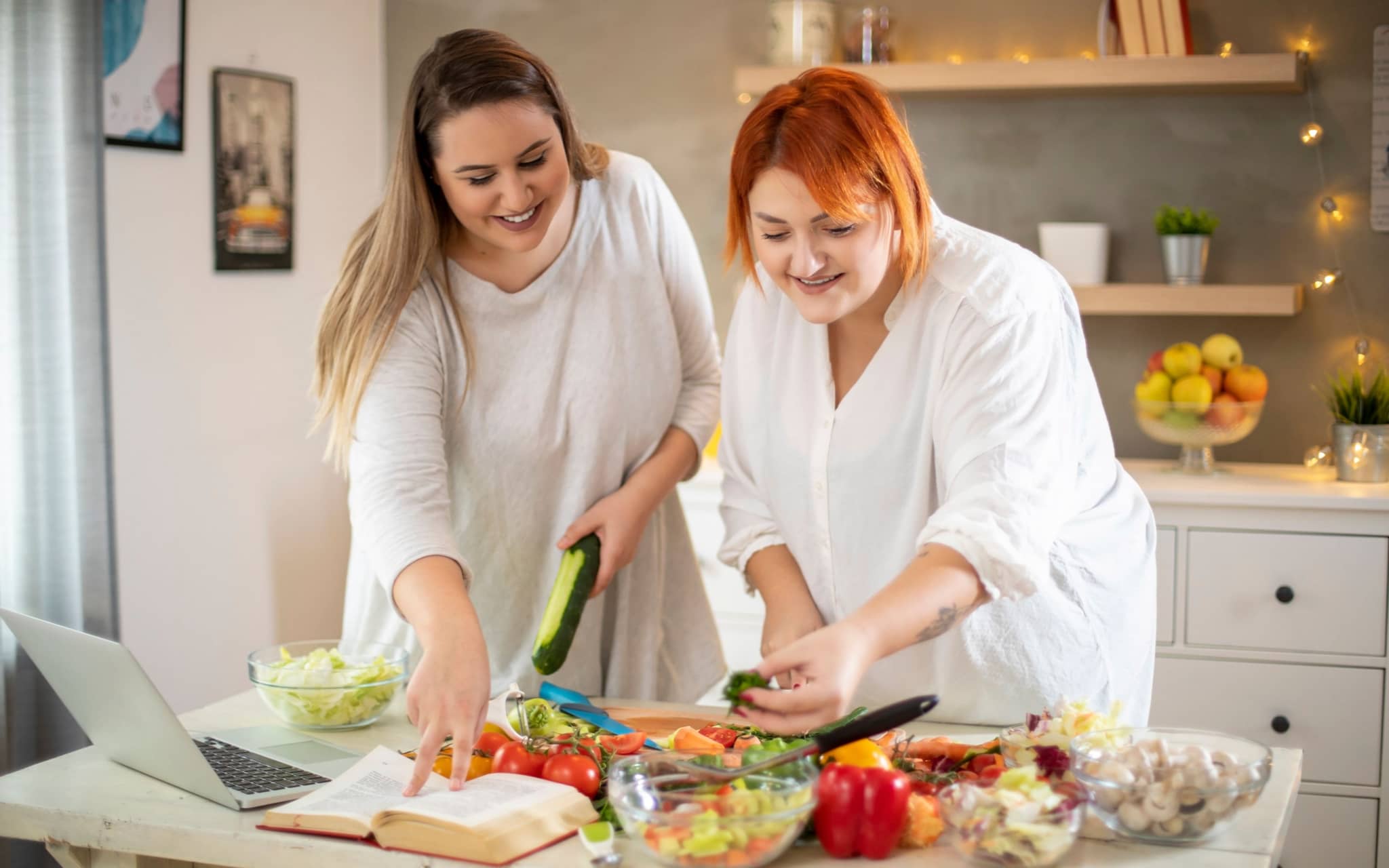Abnehmtipps vom Ernährungsmediziner: Zwei Frauen mit Übergewicht kochen gesundes Essen nach Anleitung