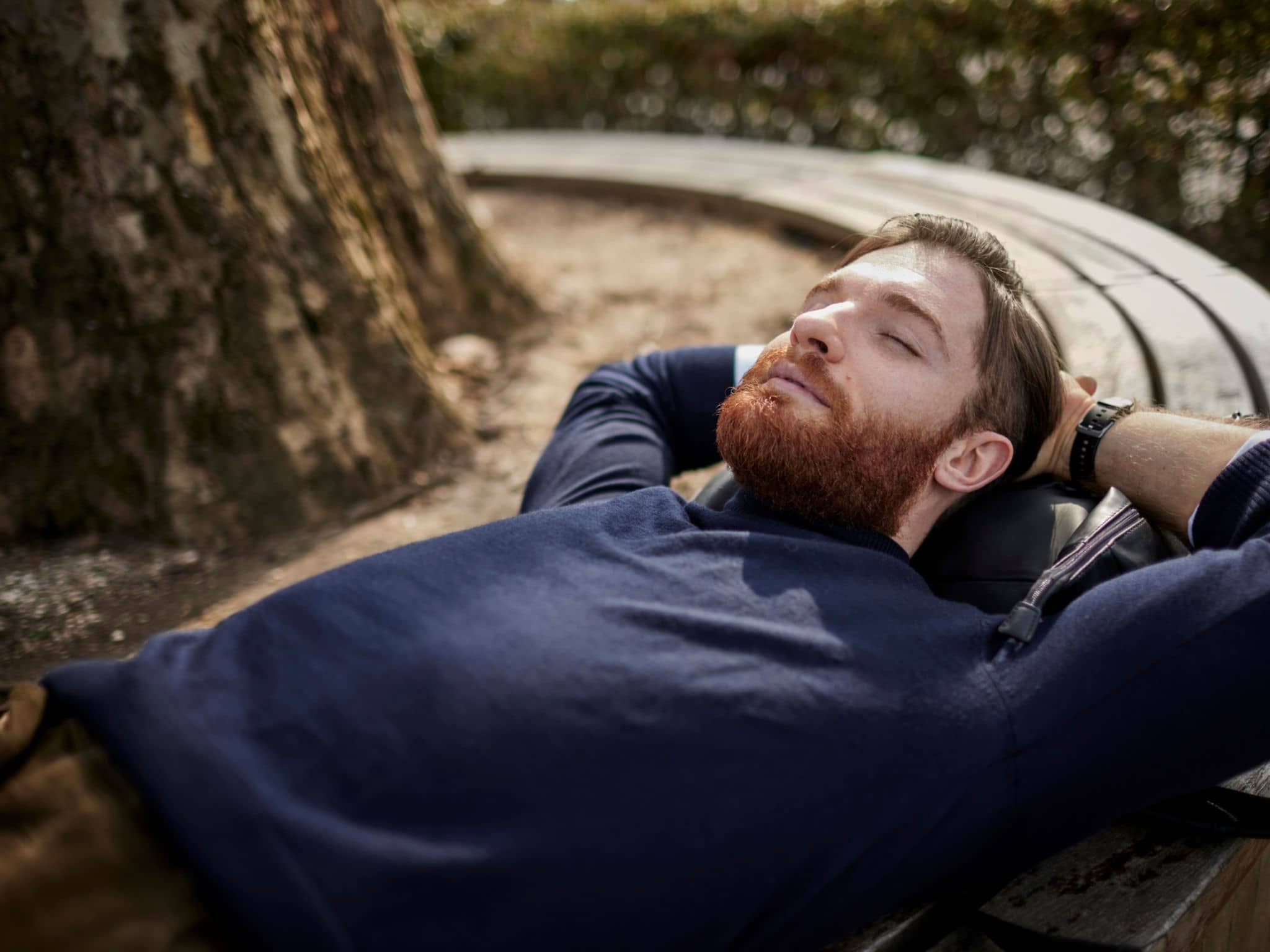 Kraftquellen finden: Mann liegt mit geschlossenen Augen und verschränkten Armen hinter dem Kopf auf einer runden Baumbank.