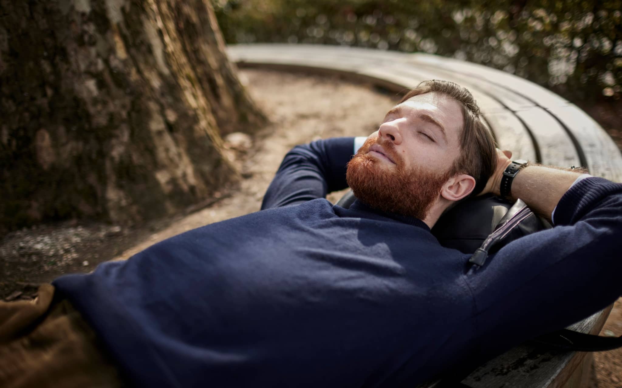 Kraftquellen finden: Mann liegt mit geschlossenen Augen und verschränkten Armen hinter dem Kopf auf einer runden Baumbank.