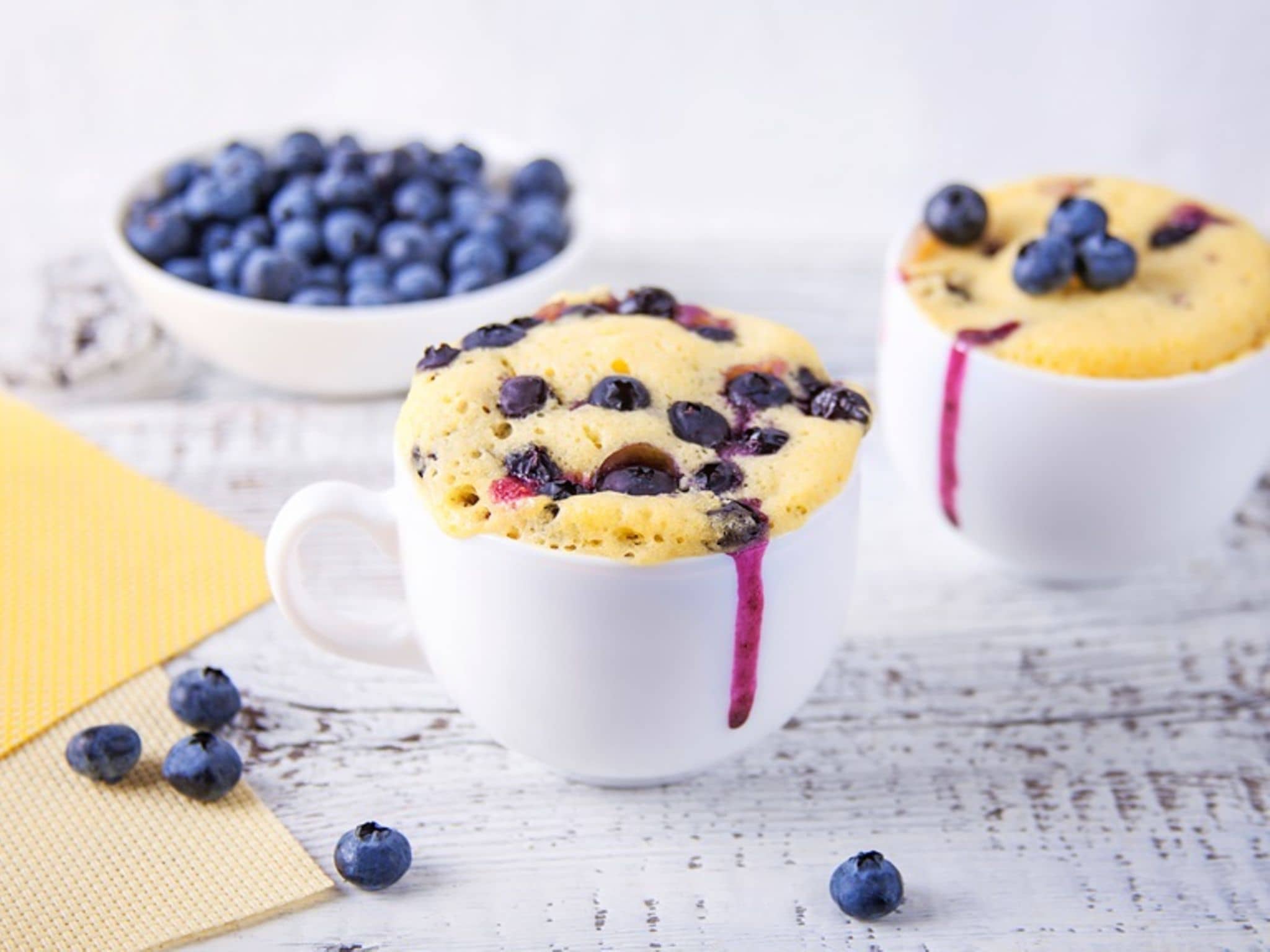 Beeren-Tassenkuchen: Zwei Tassen mit Blaubeer-Kuchen und eine Schale mit Blaubeeren