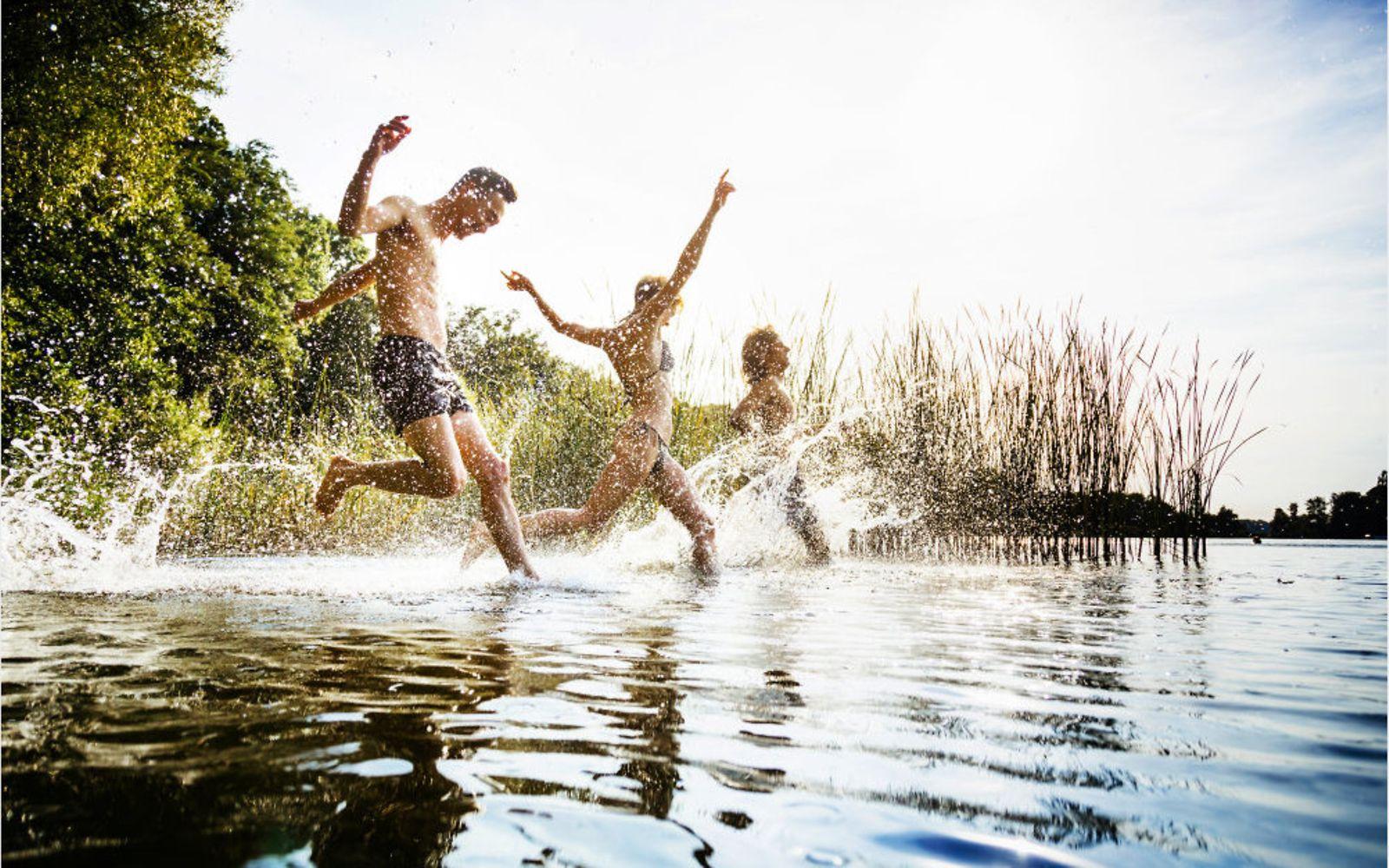 Bewegung und Sport: Drei Personen laufen in einen See.