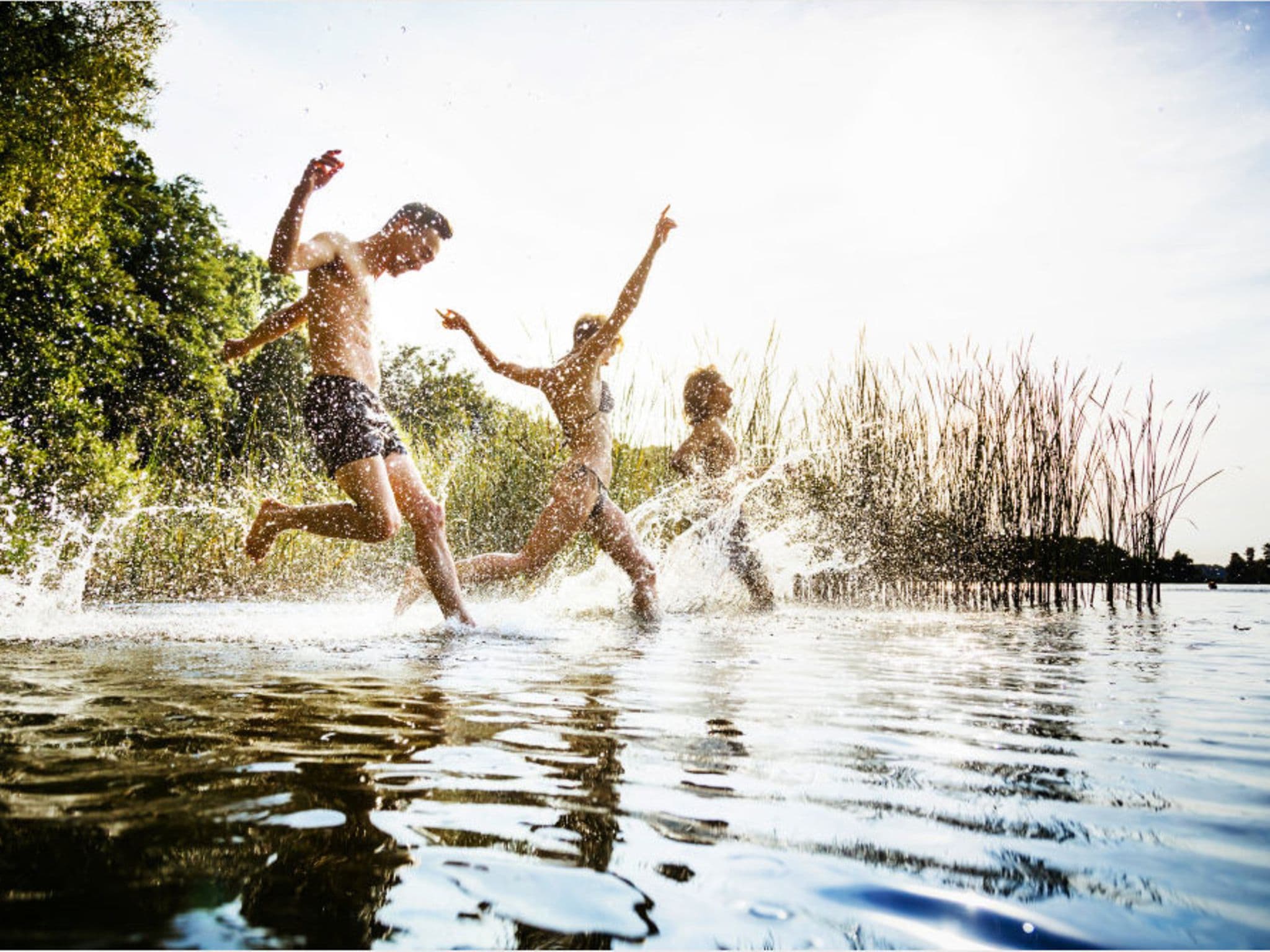 Bewegung und Sport: Drei Personen laufen in einen See.