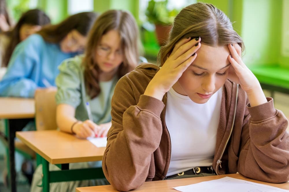 Jugendliches Mädchen mit Prüfungsangst sitzt ängstlich über einer Klausur.