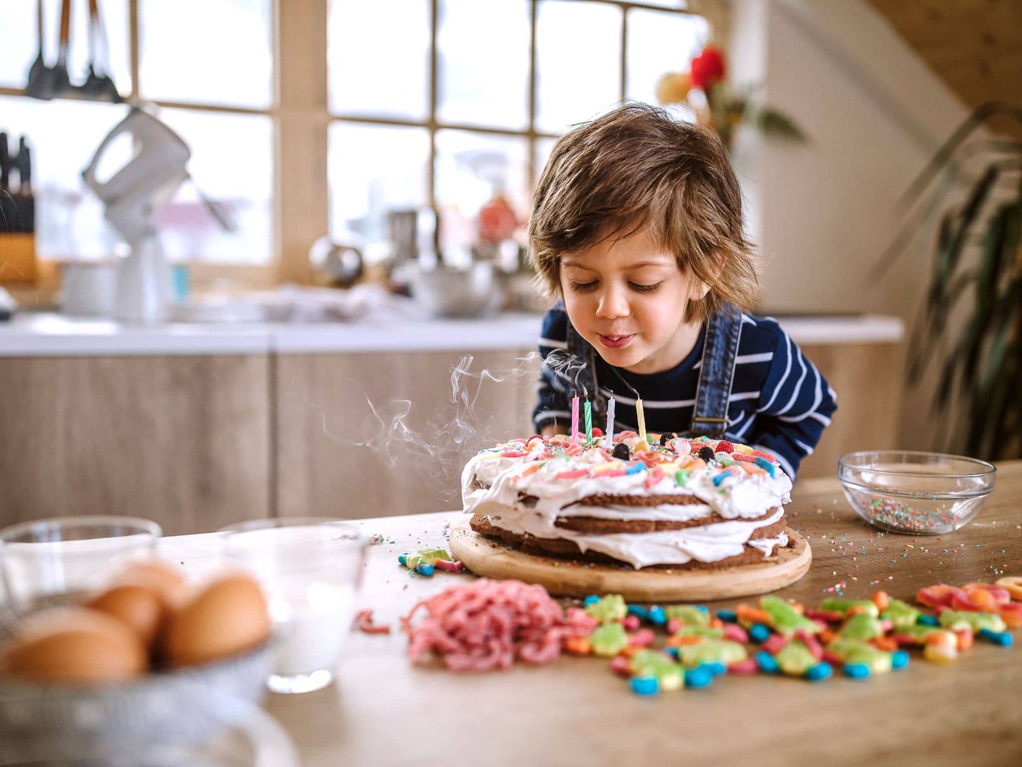 Ein Kind pustet die Kerzen auf einem selbst gebackenen Geburtstagskuchen aus.