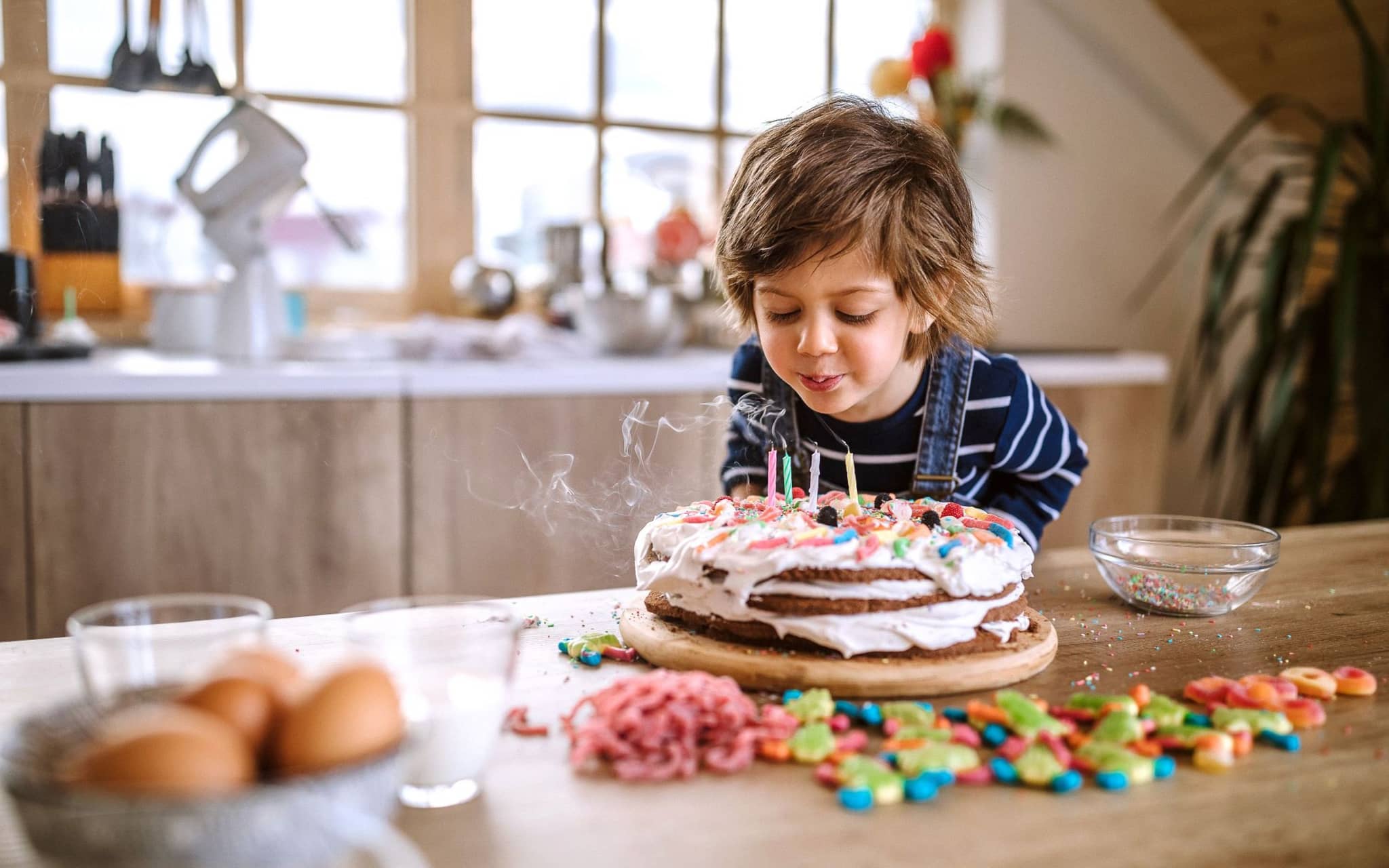 Ein Kind pustet die Kerzen auf einem selbst gebackenen Geburtstagskuchen aus.