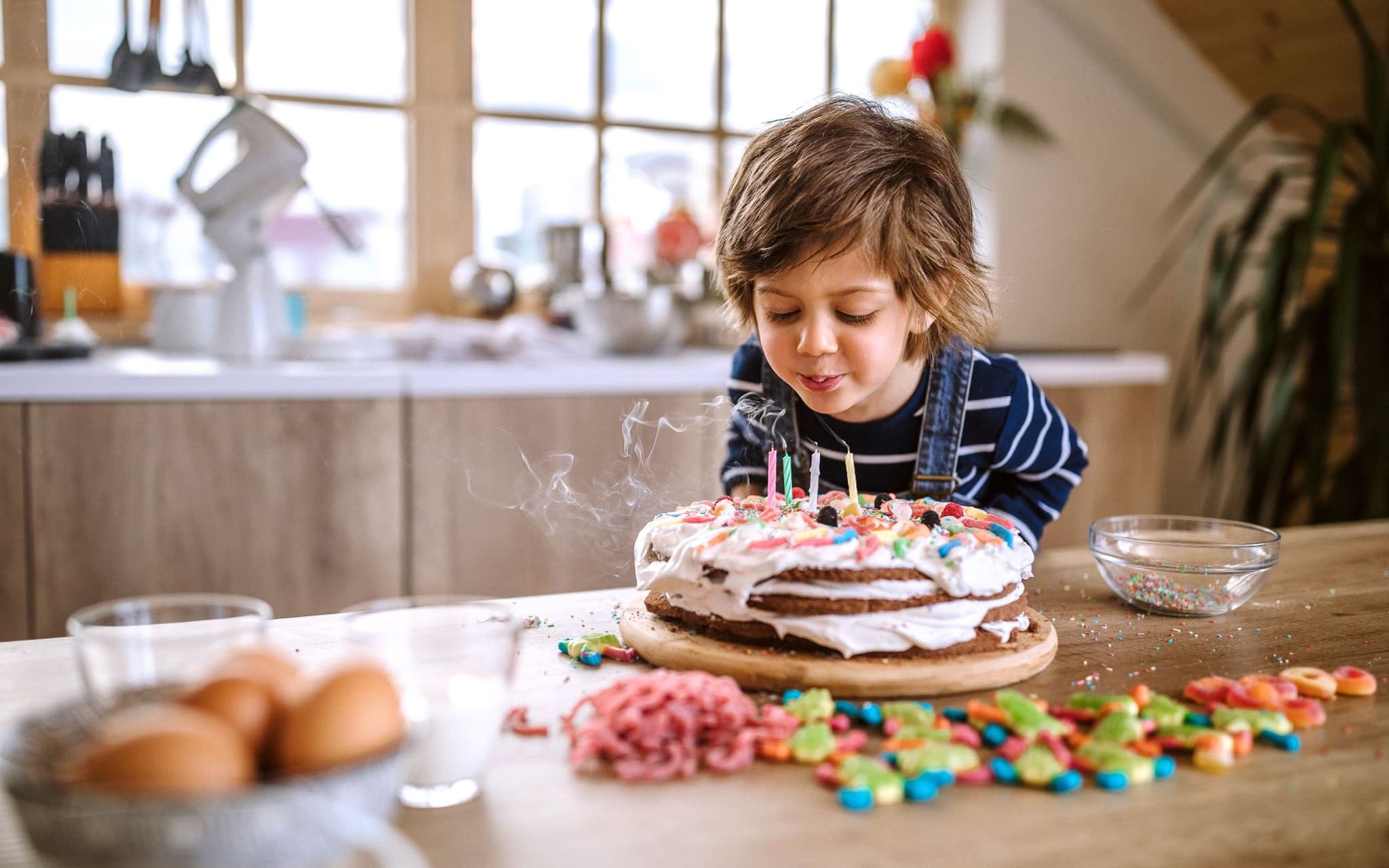Ein Kind pustet die Kerzen auf einem selbst gebackenen Geburtstagskuchen aus.