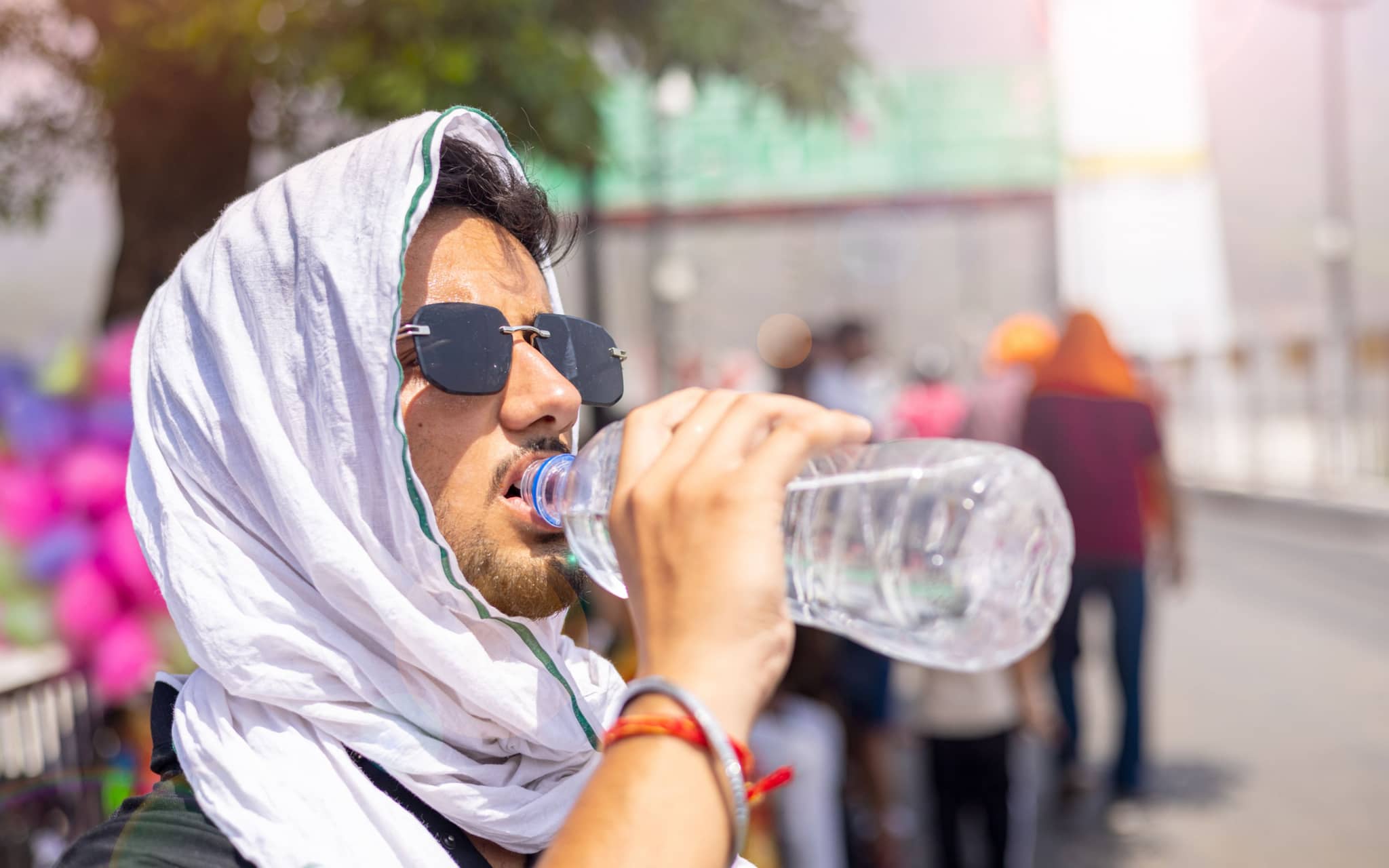 Junger Mann schützt sich vor Sonne und Hitze mit einem weißen Kopftuch und trinkt Wasser aus einer Flasche.