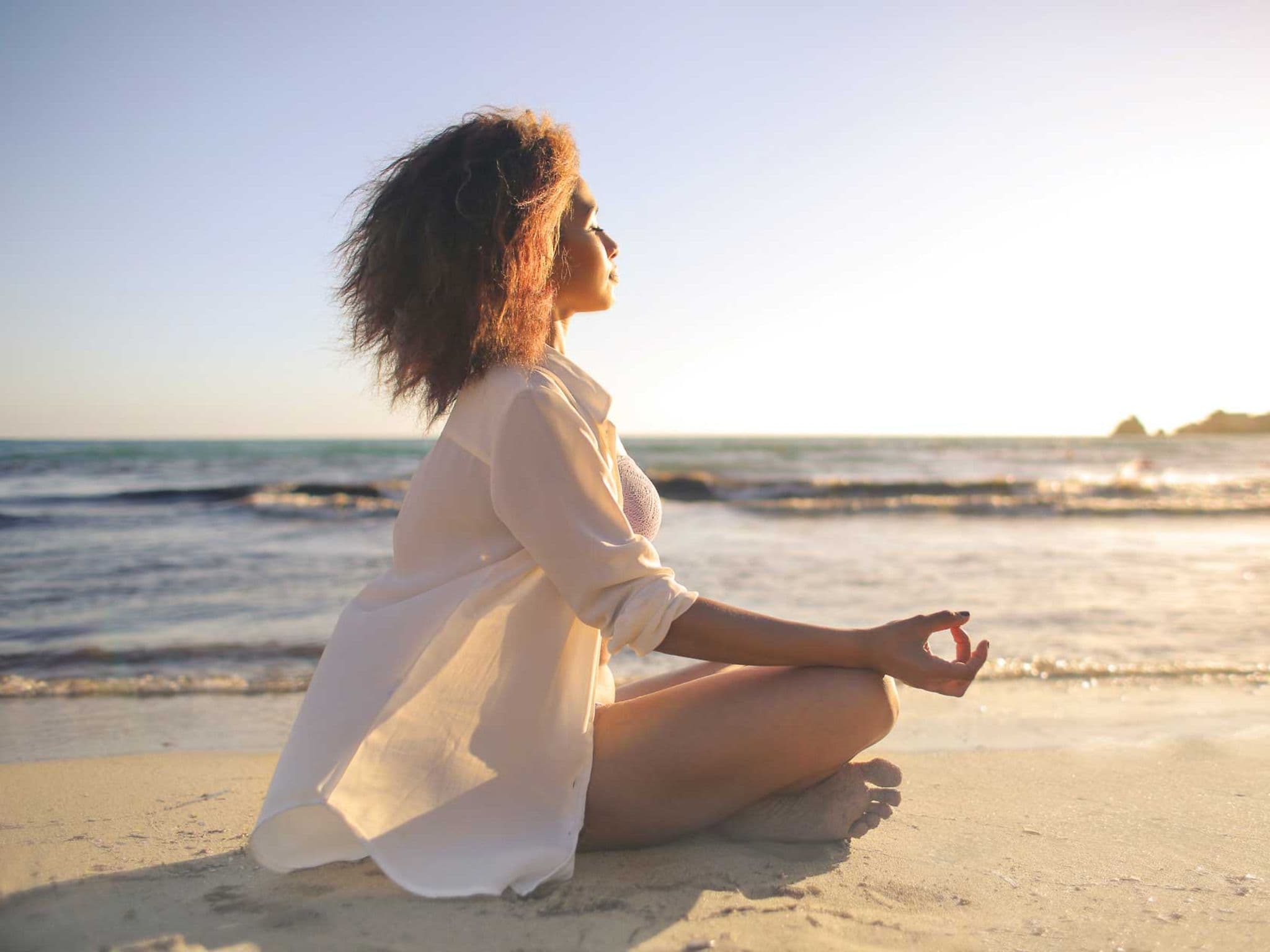 Frau sitzt meditierend am Strand und genießt die warme Meeresbrise