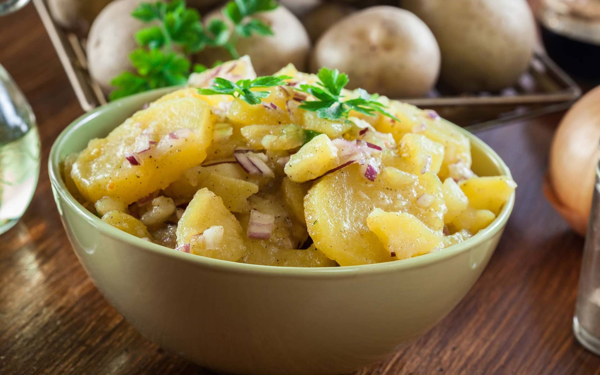 Rezeptfoto: Schüssel mit Kartoffelsalat. Daneben liegen rohe Kartoffeln.