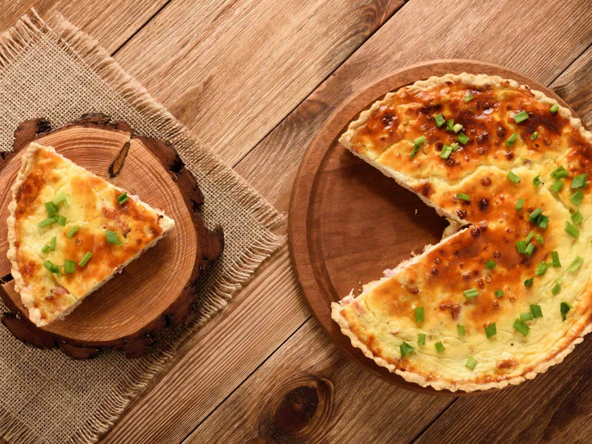 Rezeptfoto: Auf einem rustikalen Tisch stehen zwei Holzteller mit Süßkartoffel-Quiche.