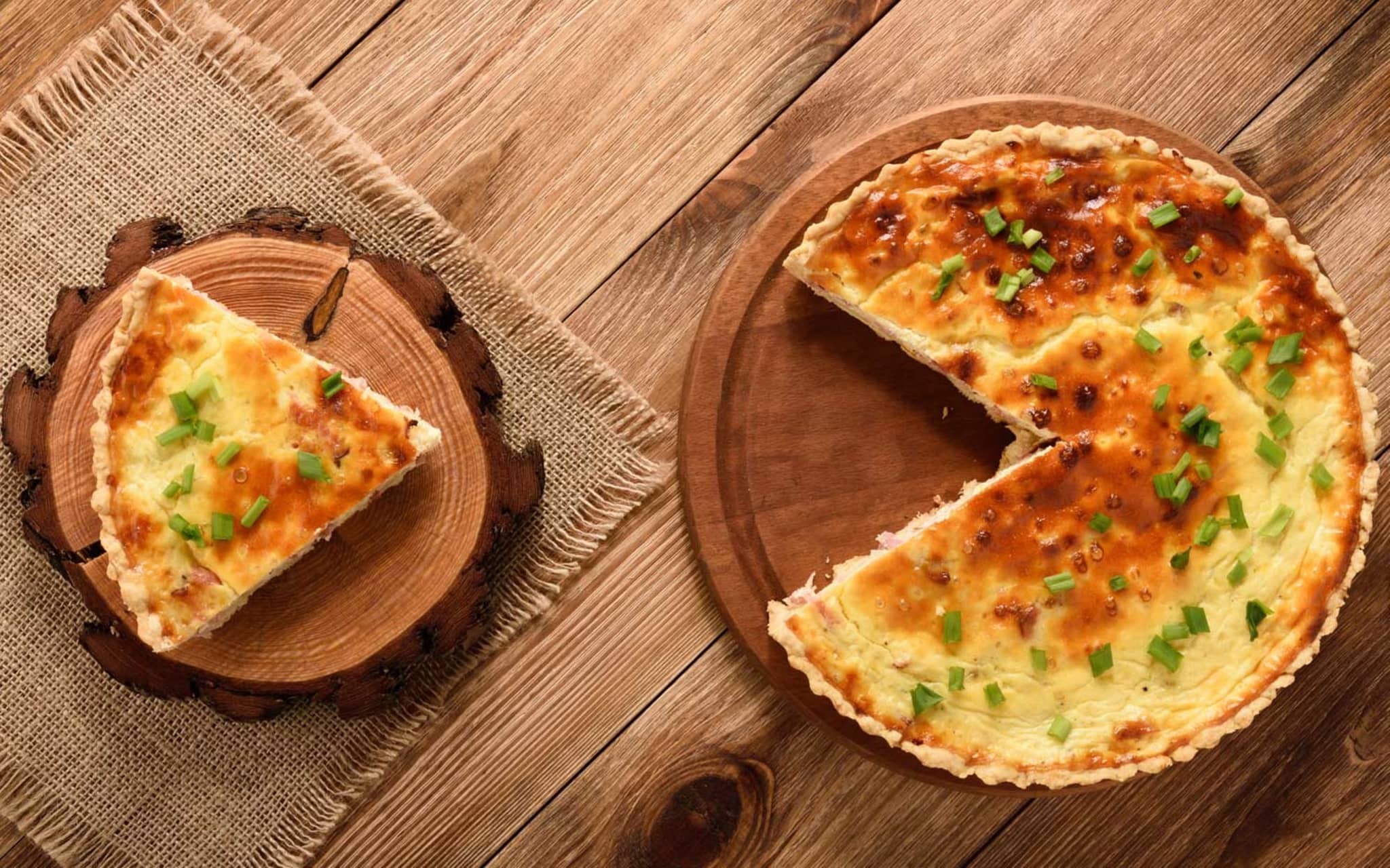 Rezeptfoto: Auf einem rustikalen Tisch stehen zwei Holzteller mit Süßkartoffel-Quiche.