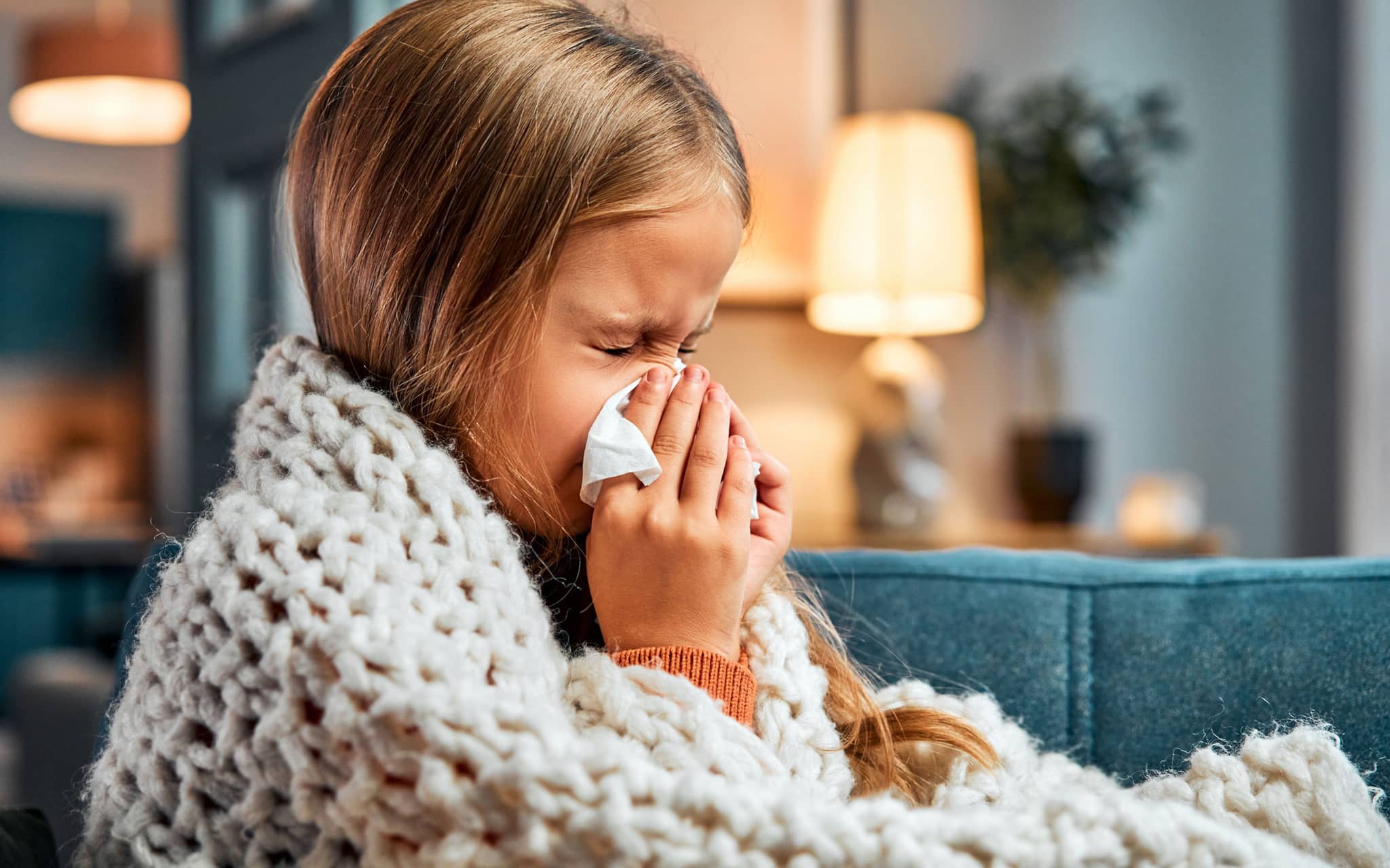Erkältung bei Kindern: Kleines Mädchen auf dem Sofa putzt sich mit einem Taschentuch die Nase.