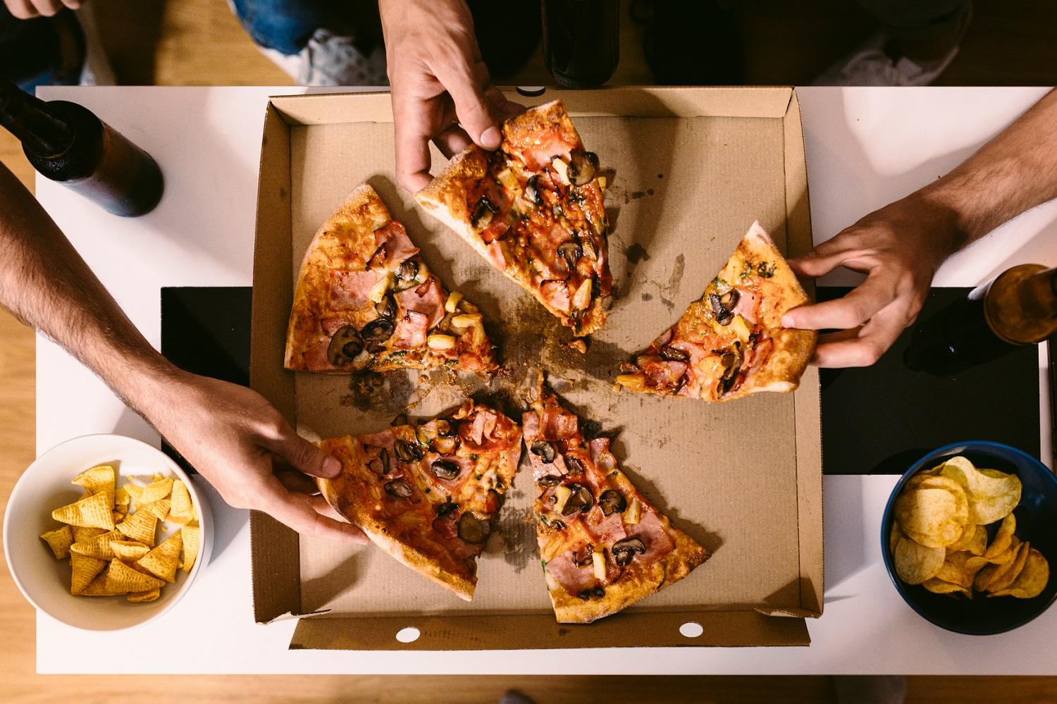 Richtige Ernährung nach dem Sport: Drei Hände greifen nach Pizzastücken in einem Karton
