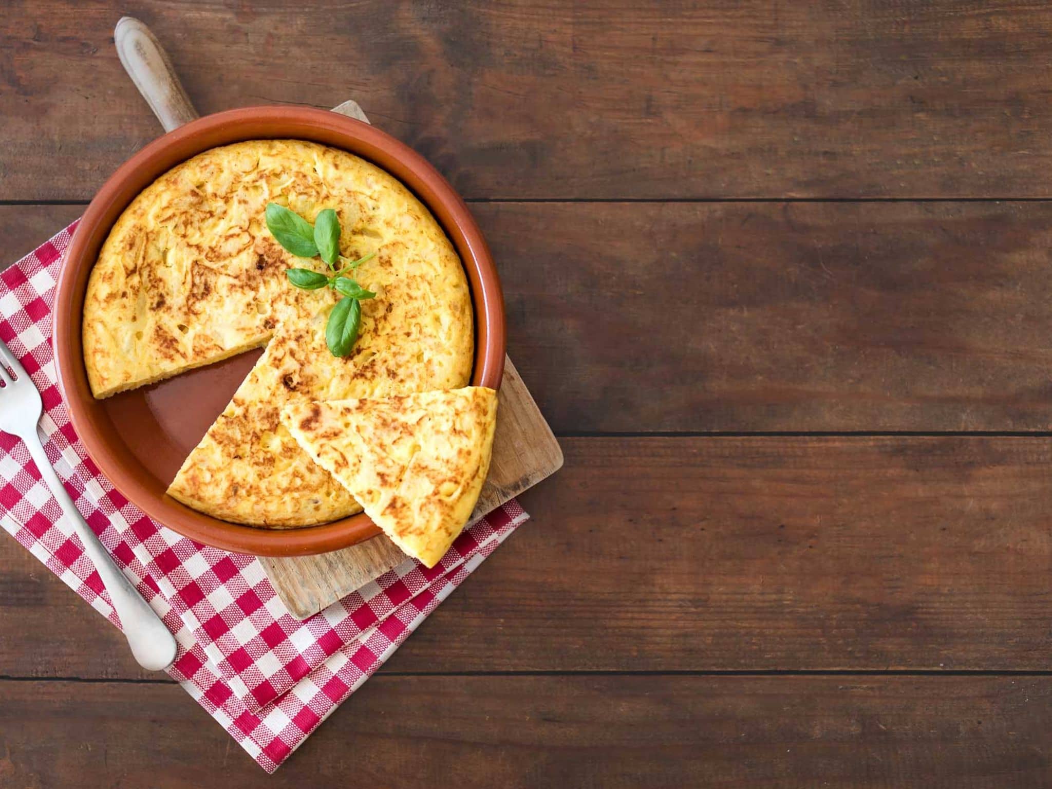 Rezeptfoto: Auf einem rustikalen Tisch steht eine spanische Tortilla in einer Tonform.