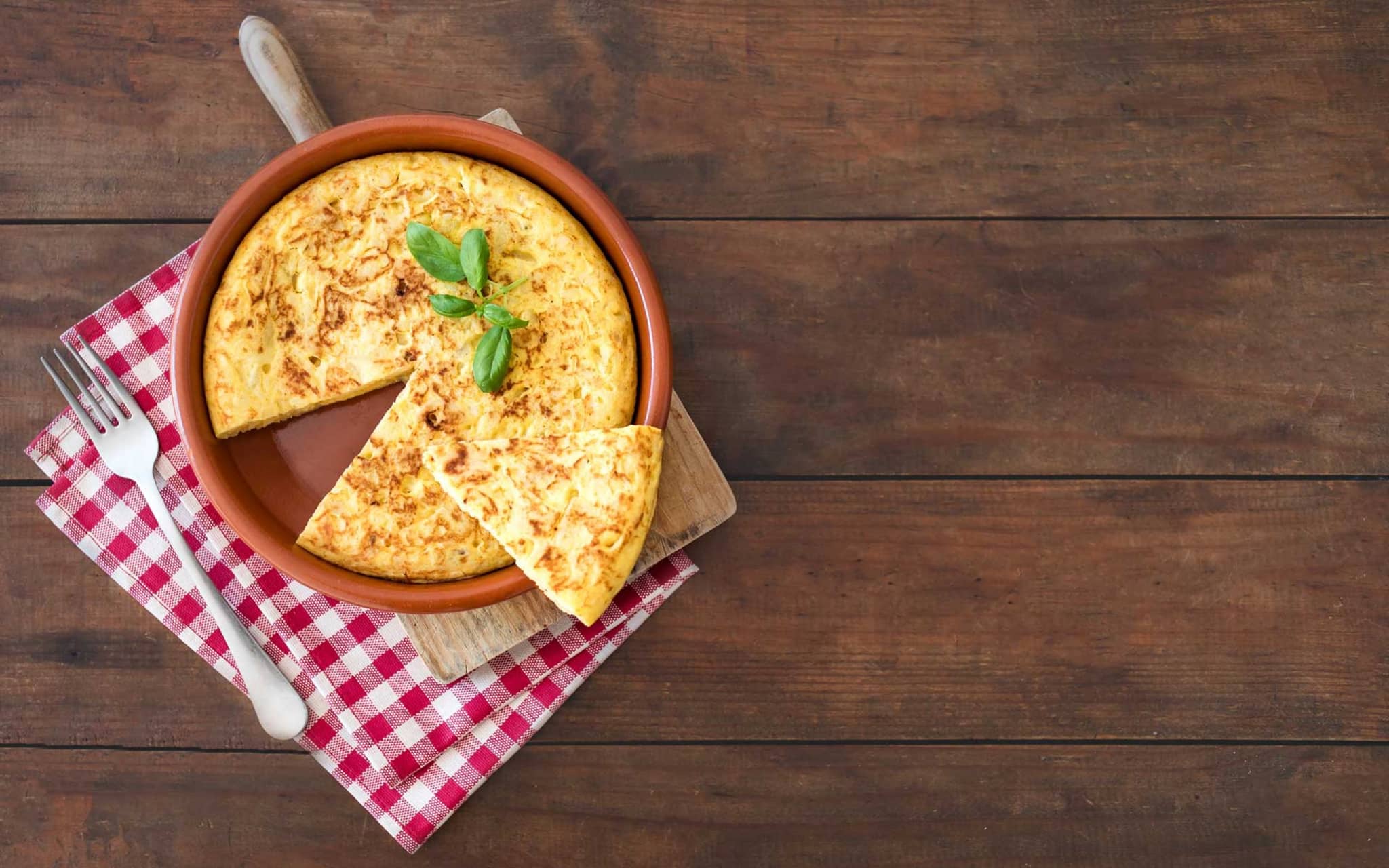 Rezeptfoto: Auf einem rustikalen Tisch steht eine spanische Tortilla in einer Tonform.