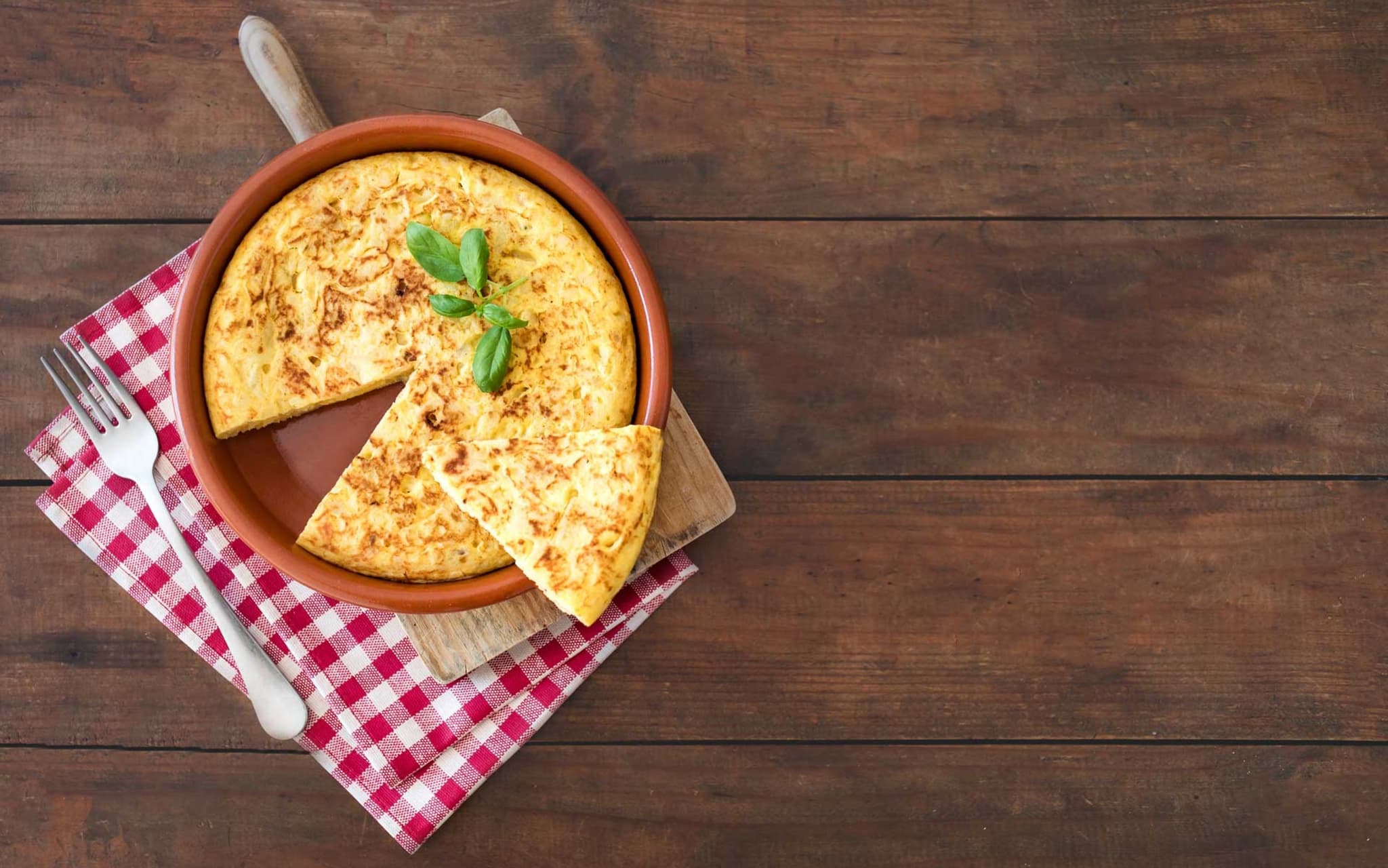 Rezeptfoto: Auf einem rustikalen Tisch steht eine spanische Tortilla in einer Tonform.