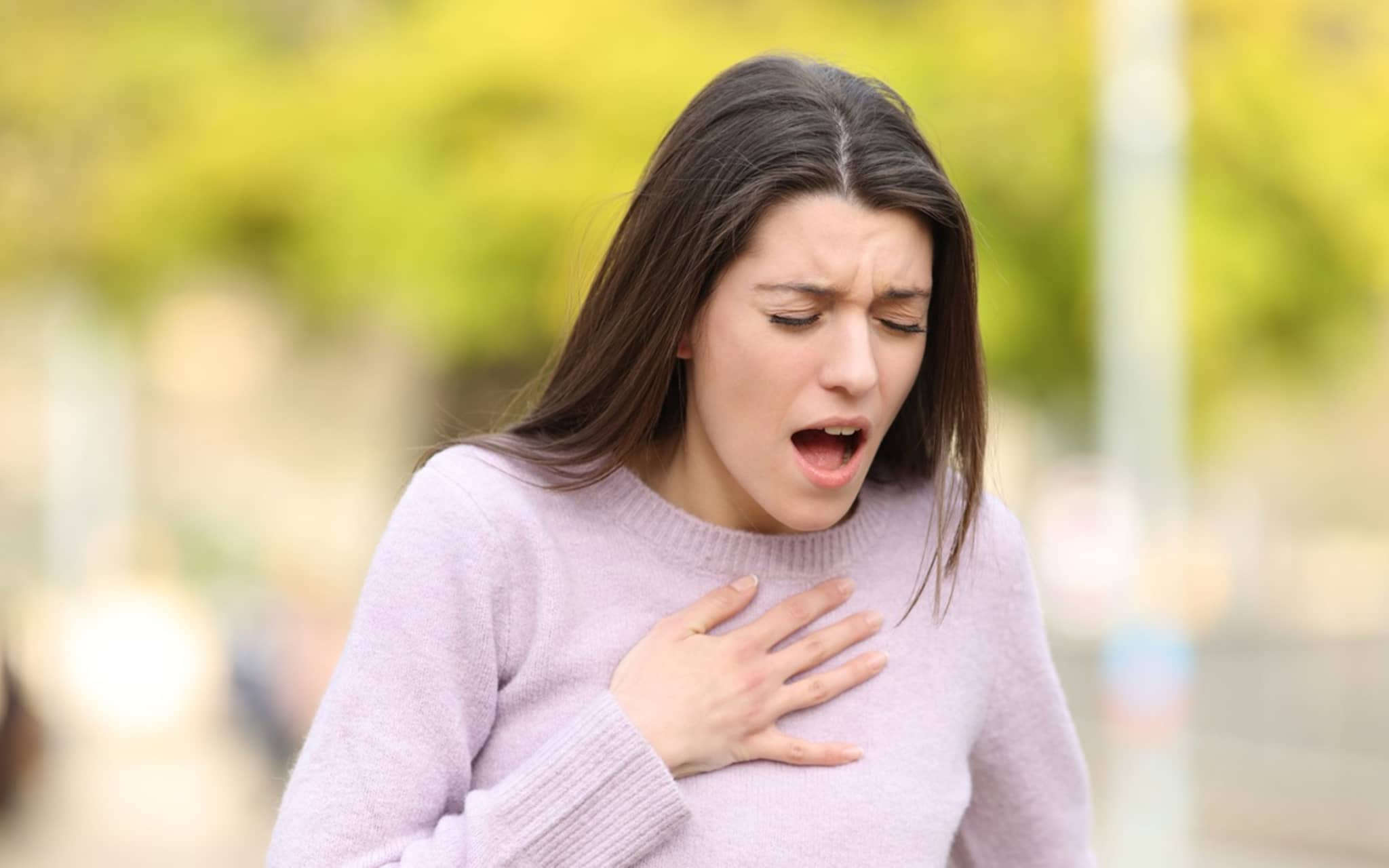 Frau mit Atemnot erlebt anaphylaktischen Schock und hält sich die Hand auf das Dekoletée.