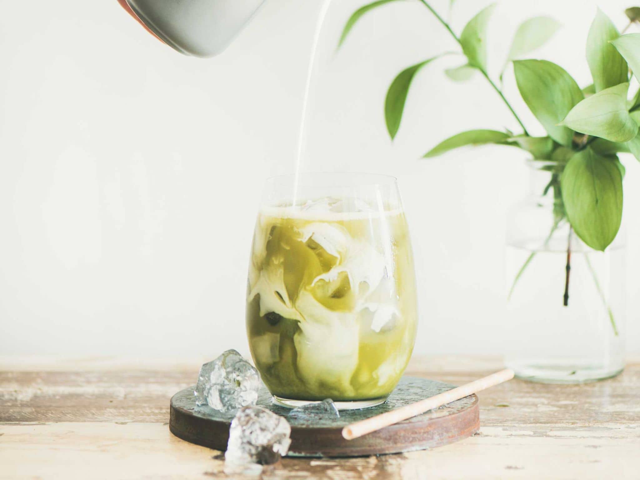 Ein Glas mit Iced Matcha, in das Milch eingegossen wird