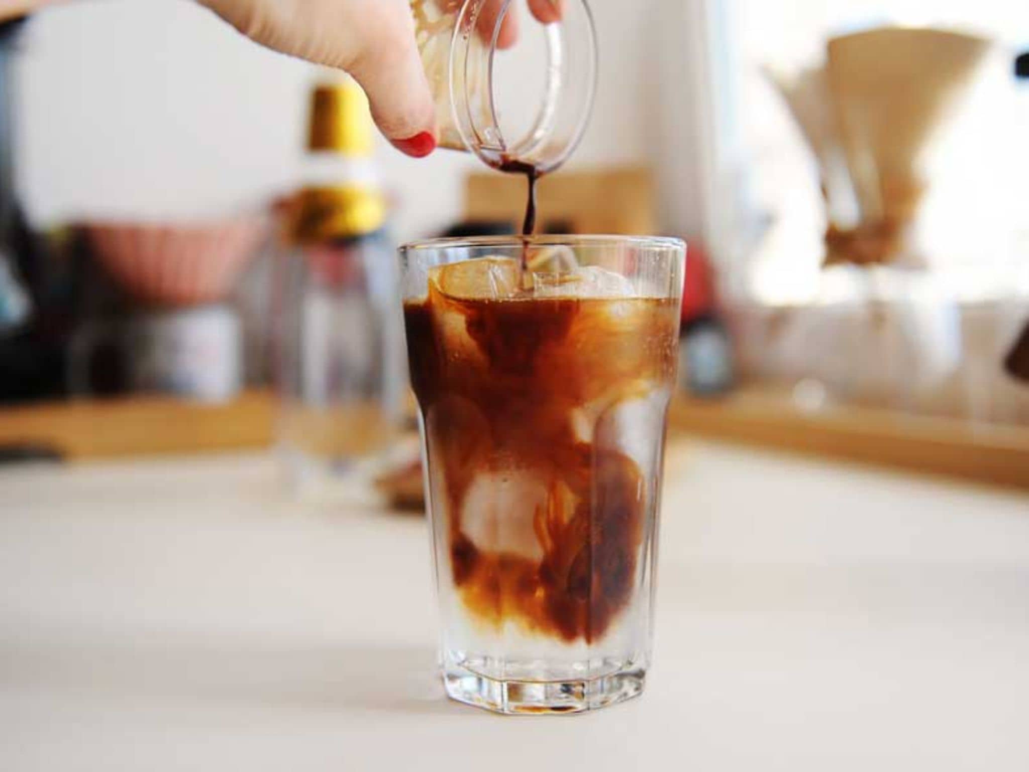 In ein Glas mit Eiswürfel gießt eine Frau Espresso