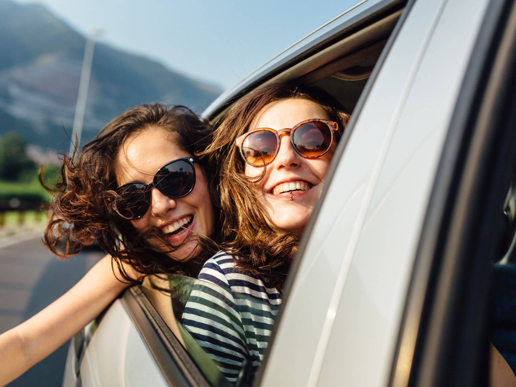 Sonnenbrille mit UV-Schutz: Zwei junge Frauen mit UV-Schutz-Sonnenbrillen schauen aus einem Auto.