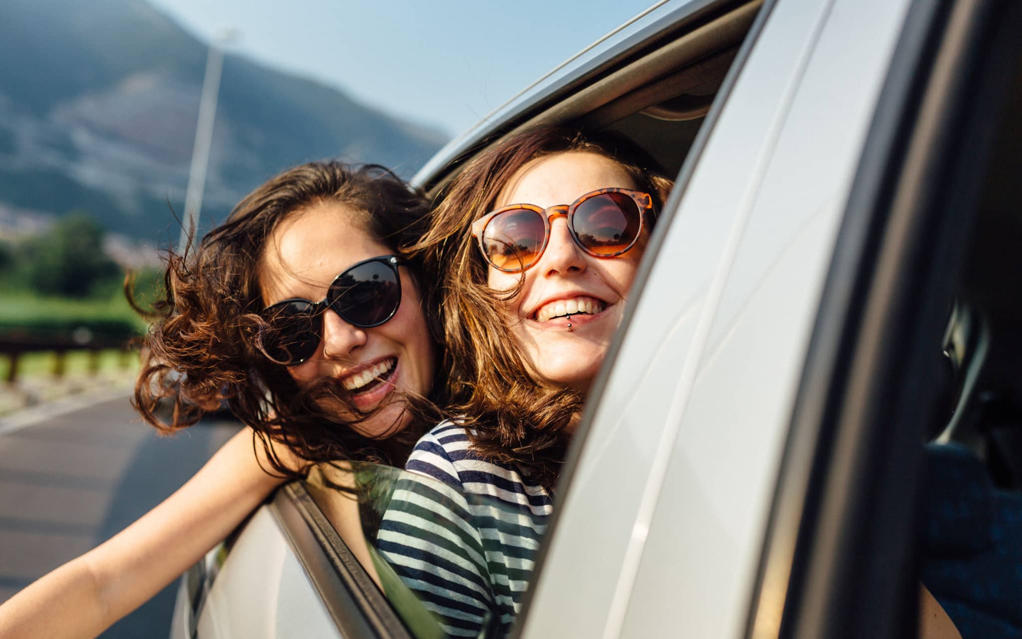 Sonnenbrille mit UV-Schutz: Zwei junge Frauen mit UV-Schutz-Sonnenbrillen schauen aus einem Auto.