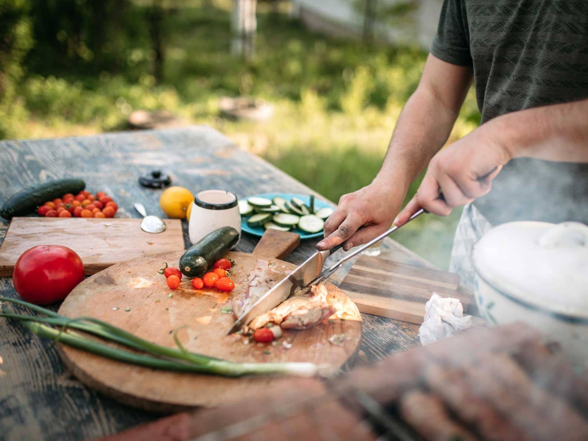 Mann schneidet Stück Fleisch auf einem Brett, das auf dem Gartentisch steht