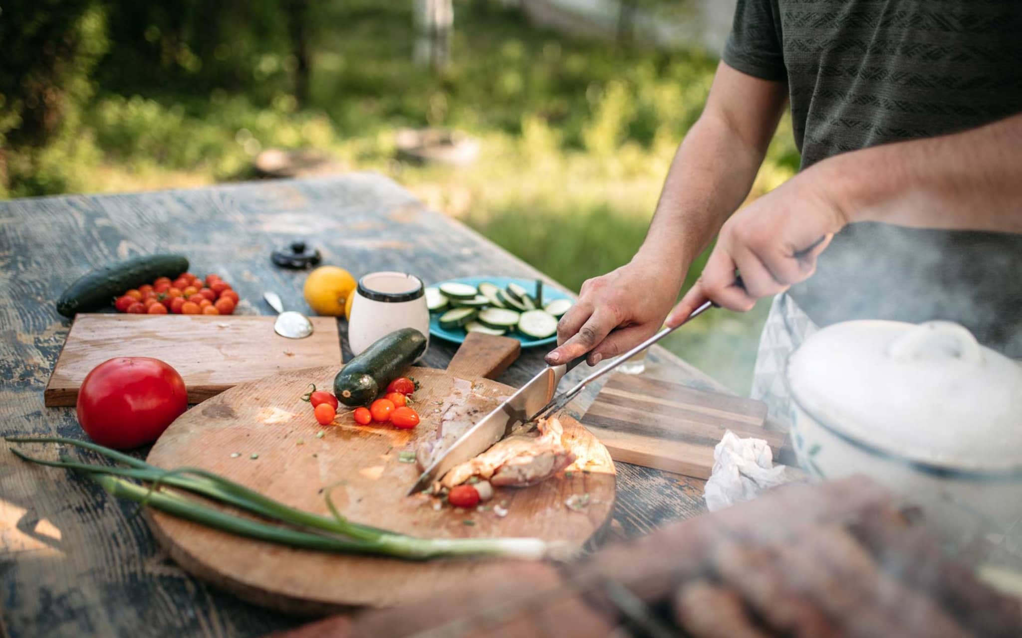 Mann schneidet Stück Fleisch auf einem Brett, das auf dem Gartentisch steht