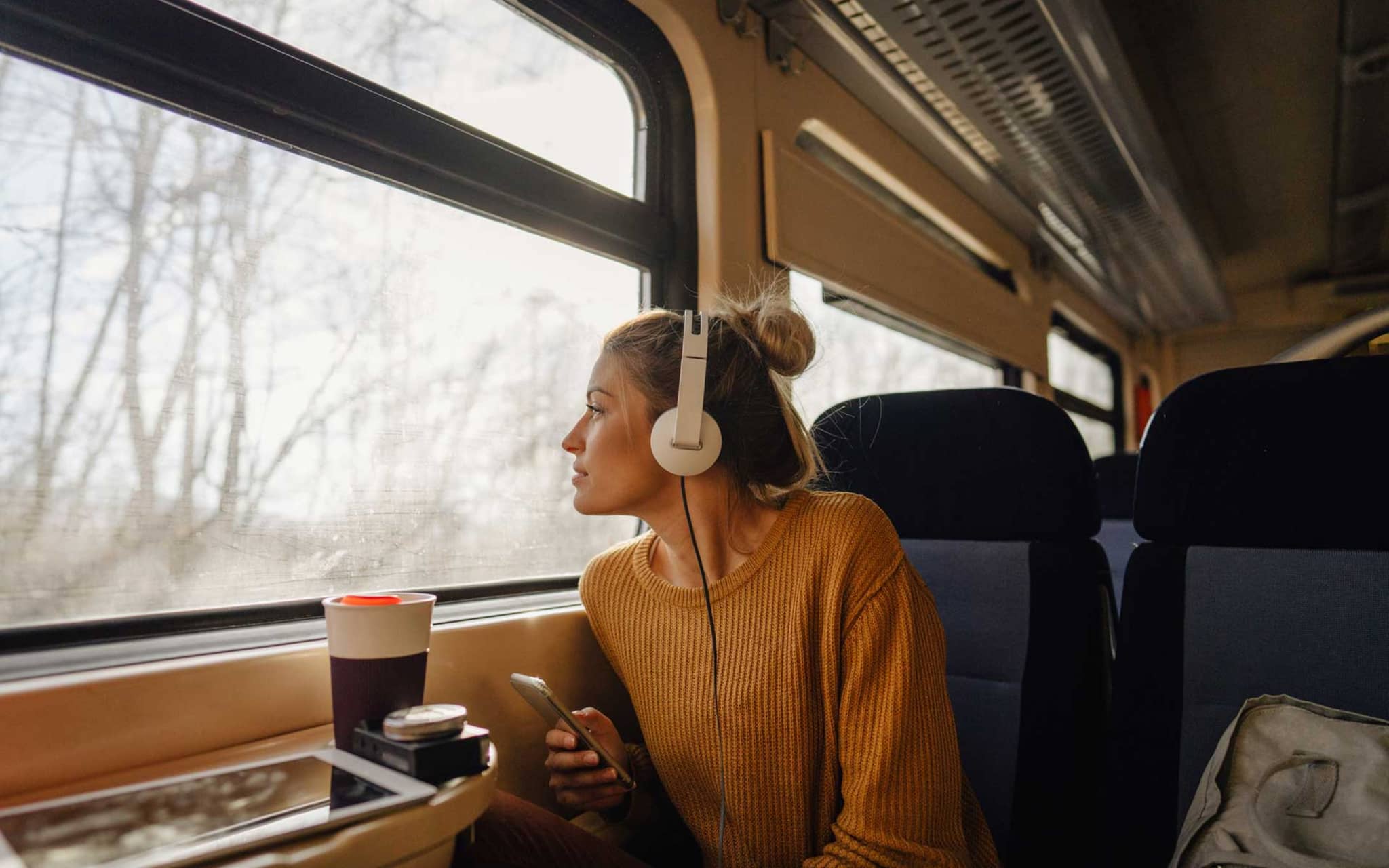 Junge Frau sitzt im Zug und hört über Kopfhörer Musik