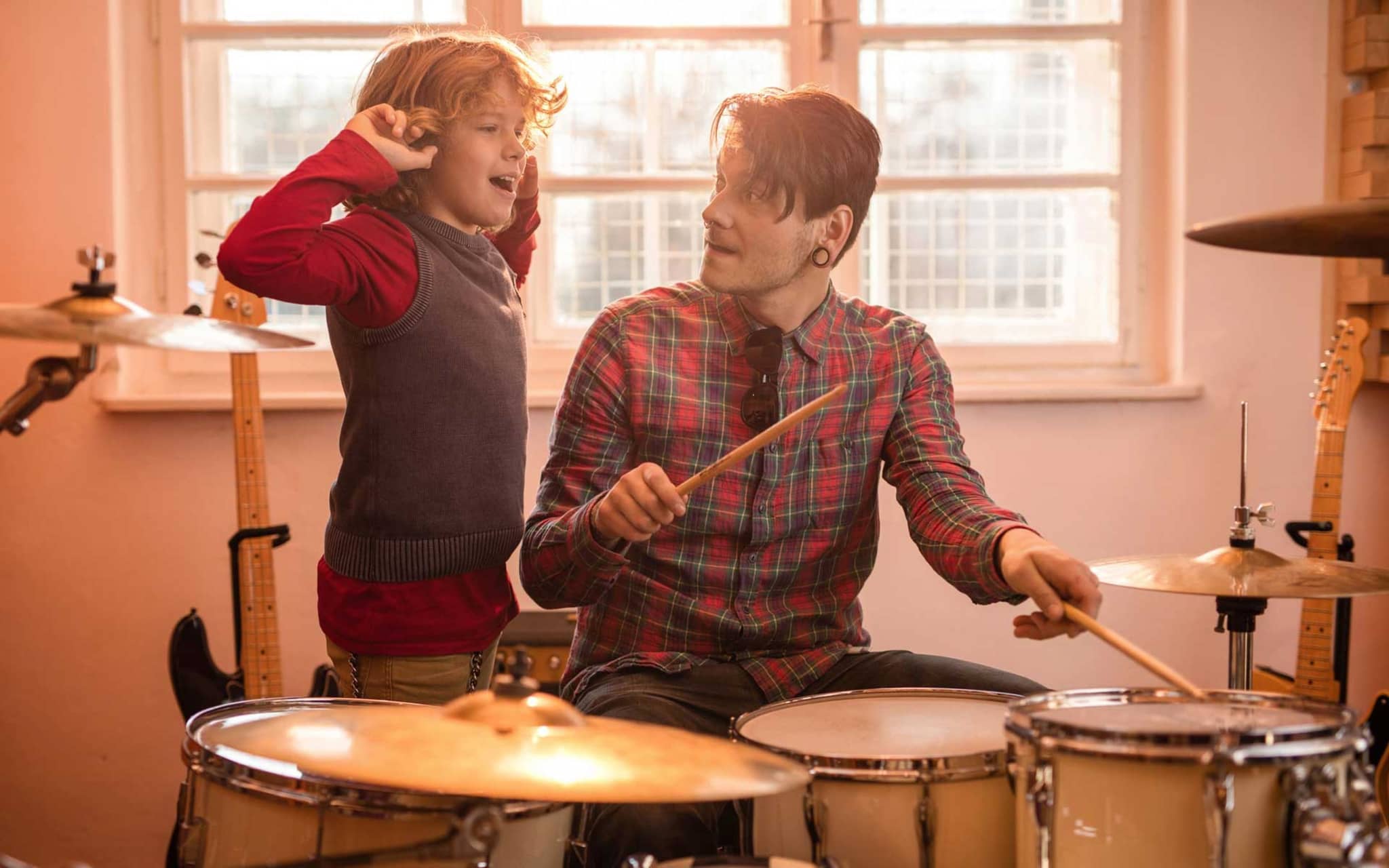 Junge hält sich die Ohren zu, während Vater Schlagzeug spielt