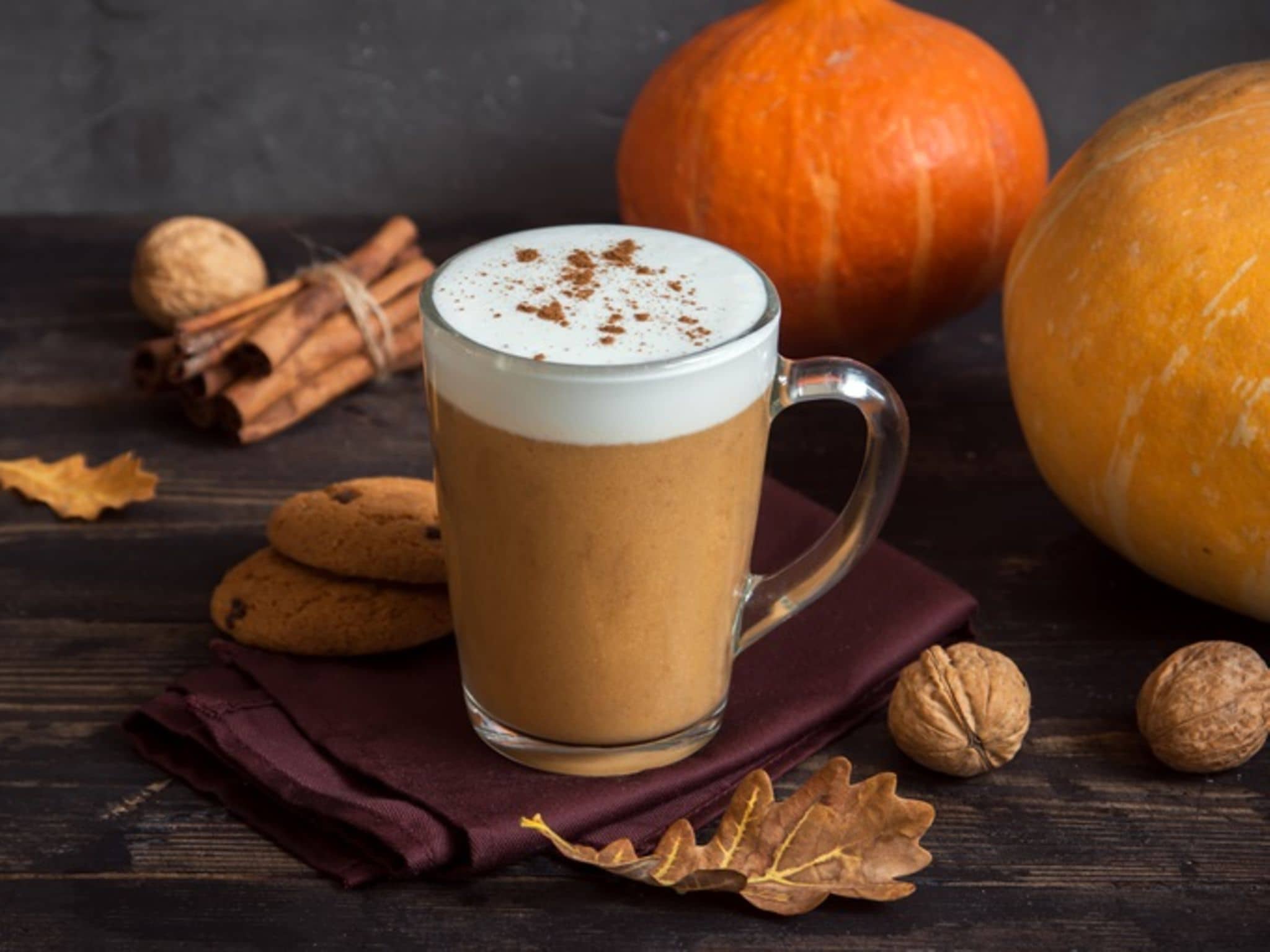 Pumpkin Spice Latte: Glas mit Pumpkin Spice Latte drin - im Hintergrund Kürbise