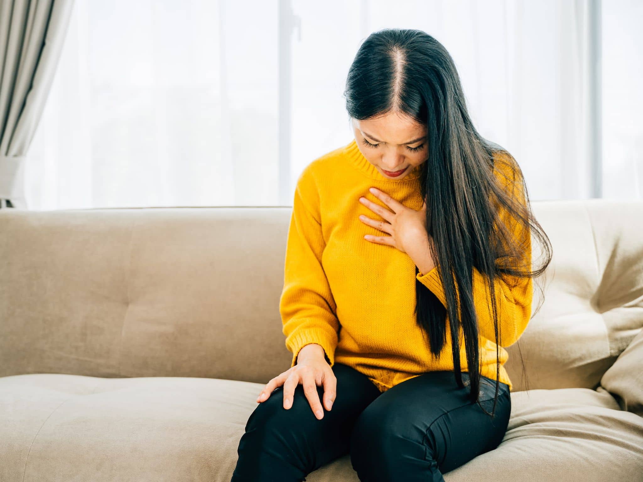 Sodbrennen Hausmittel: Frau sitzt auf Sofa und hält eine Hand an der Brust