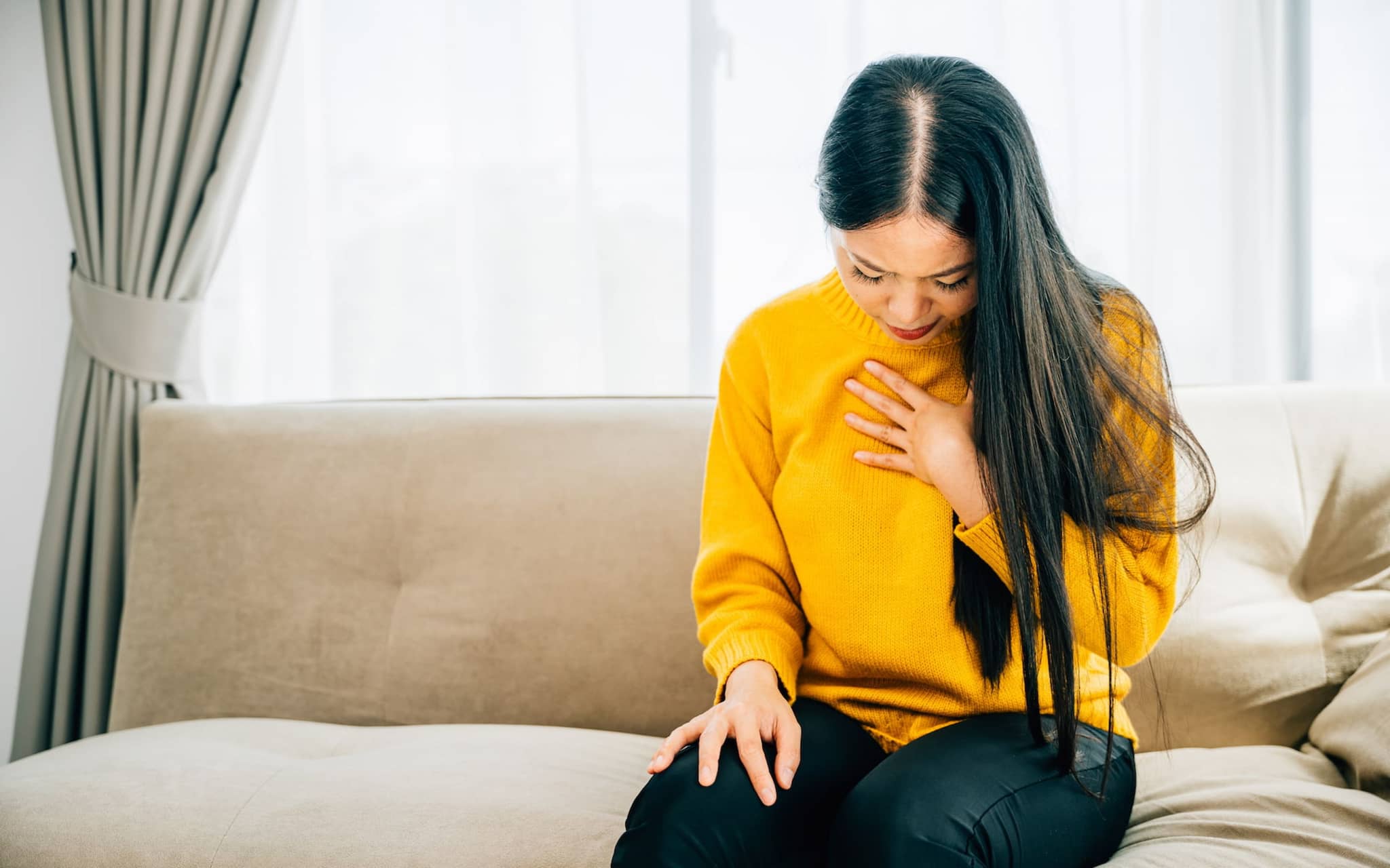 Sodbrennen Hausmittel: Frau sitzt auf Sofa und hält eine Hand an der Brust