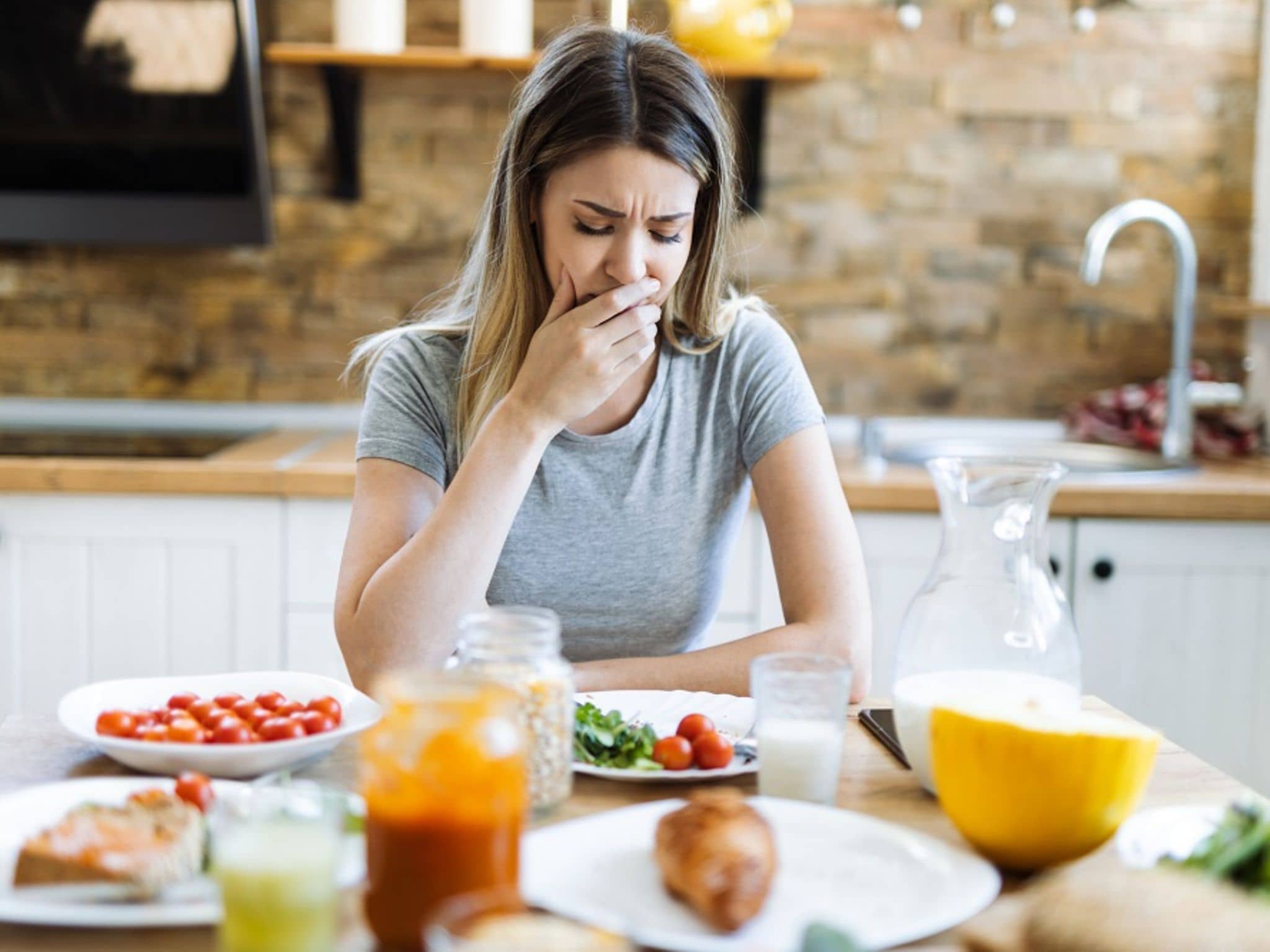 Ernährung bei Durchfall: Eine Frau sitzt am gedeckten Tisch und hat Bauchschmerzen.
