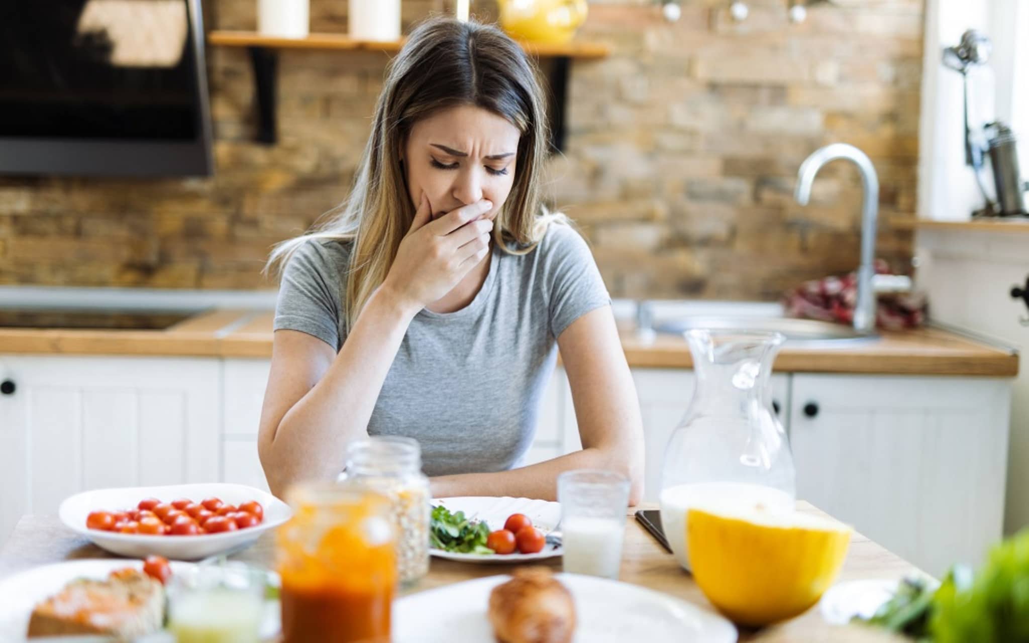 Ernährung bei Durchfall: Eine Frau sitzt am gedeckten Tisch und hat Bauchschmerzen.