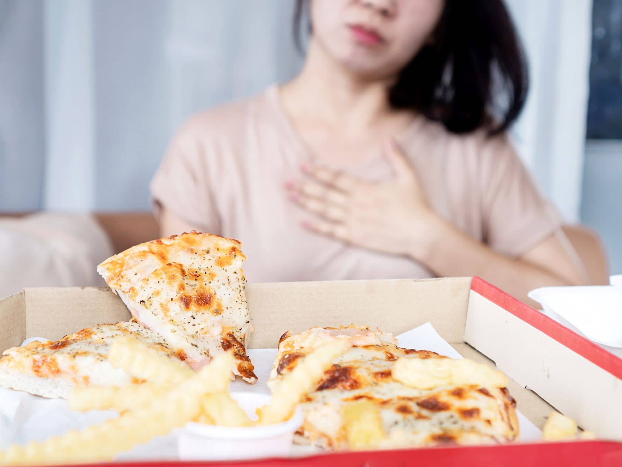 Ernährung bei Sodbrennen: Frau hält Hand auf die Brust nach Verzehr von Pizza,