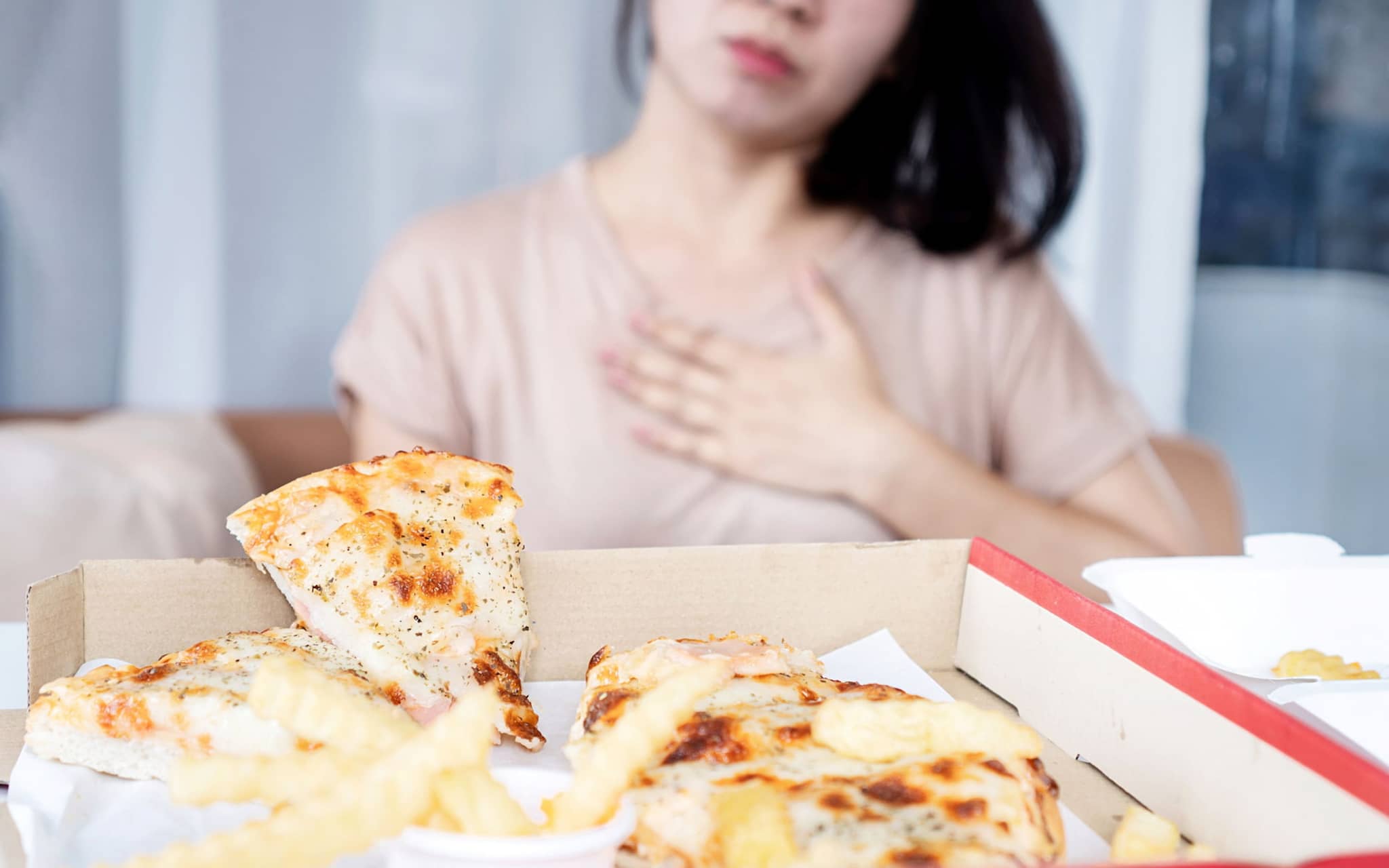 Ernährung bei Sodbrennen: Frau hält Hand auf die Brust nach Verzehr von Pizza,