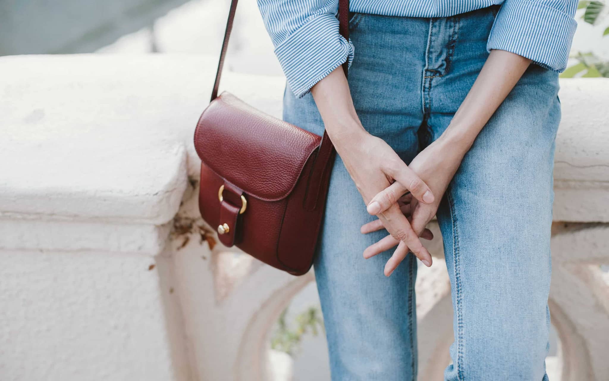 Inkontinenz: Frau in Jeans verschränkt ihre Finger vor dem Schritt.