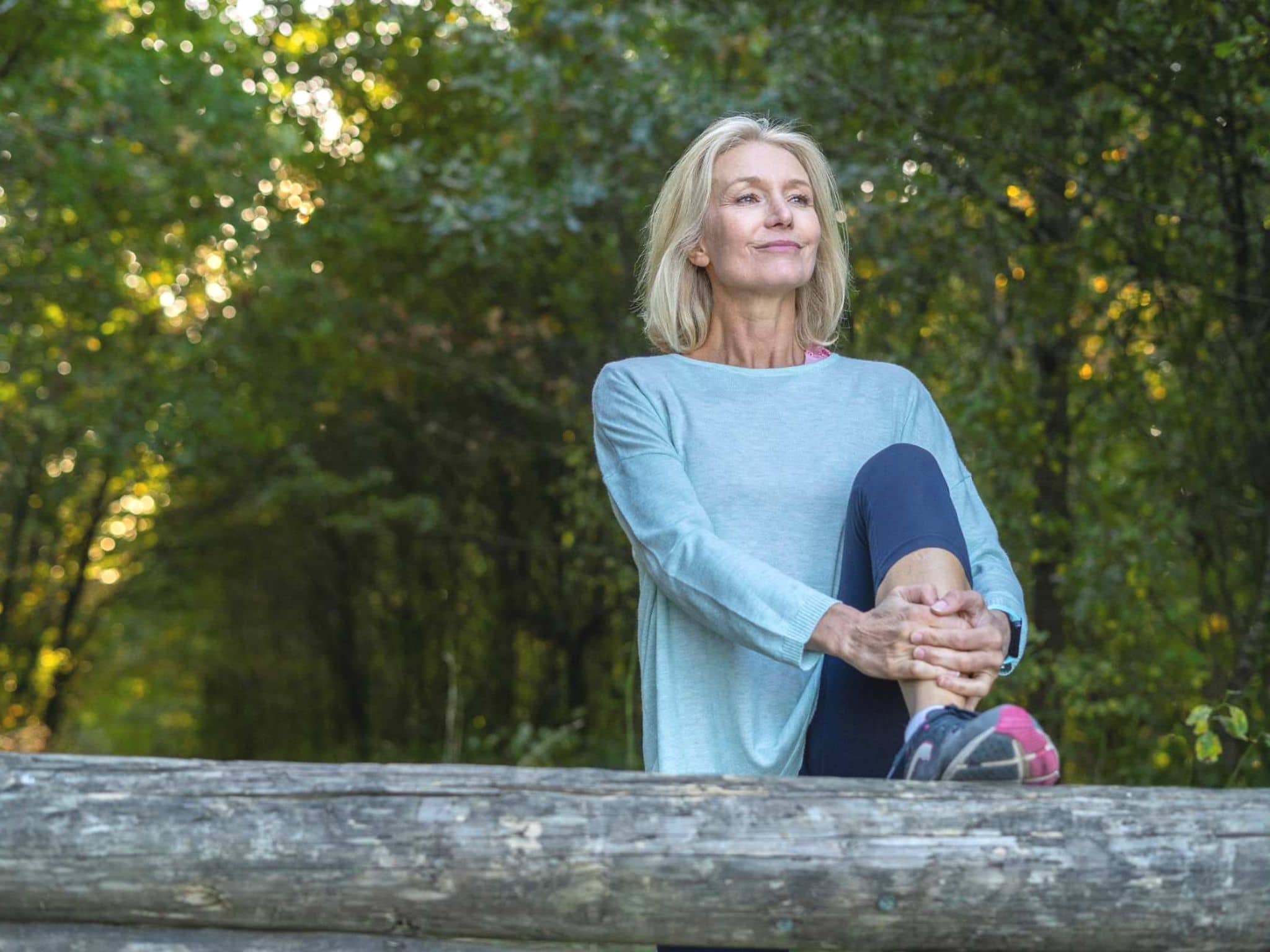 Inkontinenz bei Frauen: Lachende Frau stretcht ihr Bein im Wald.