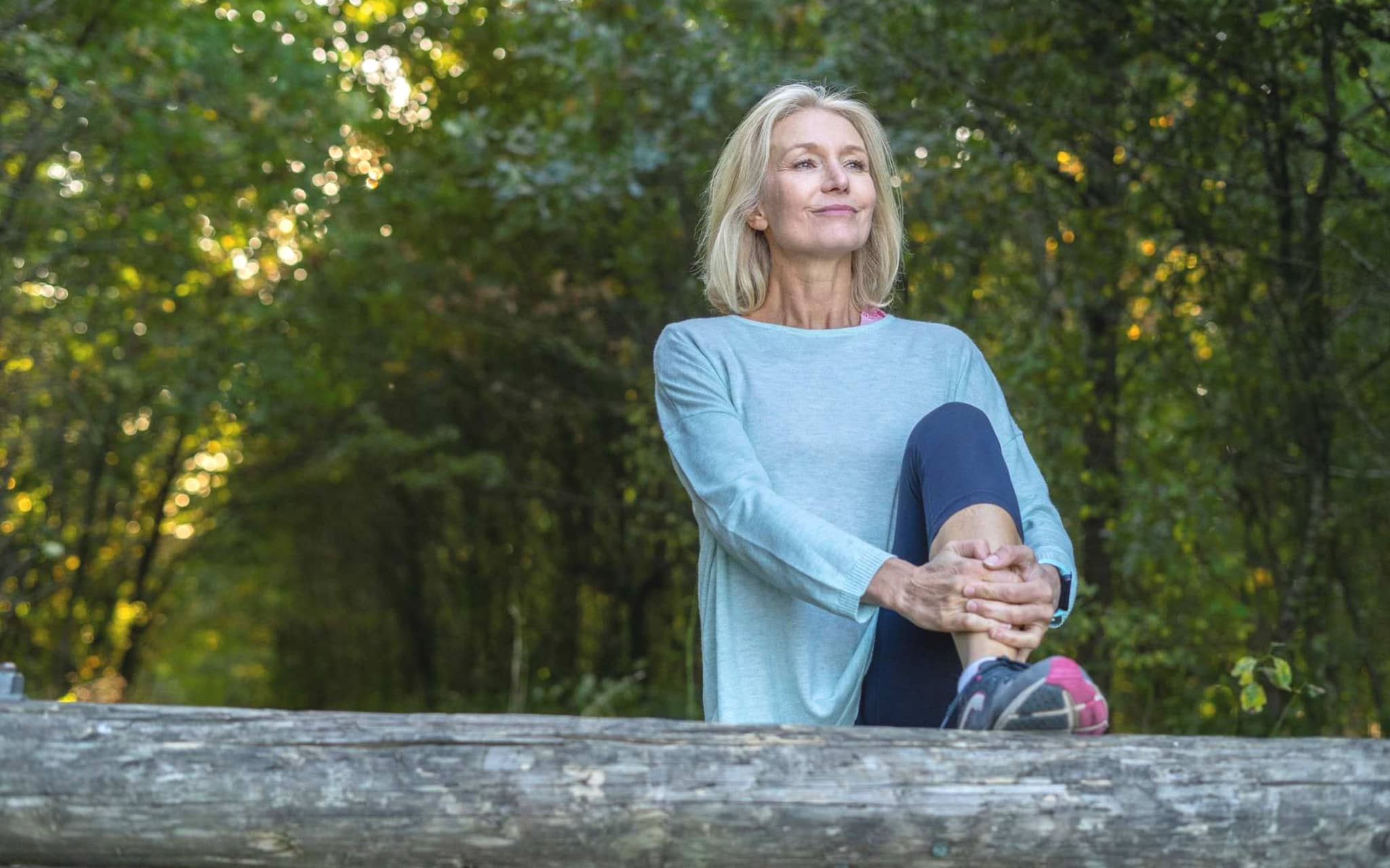 Inkontinenz bei Frauen: Lachende Frau stretcht ihr Bein im Wald.