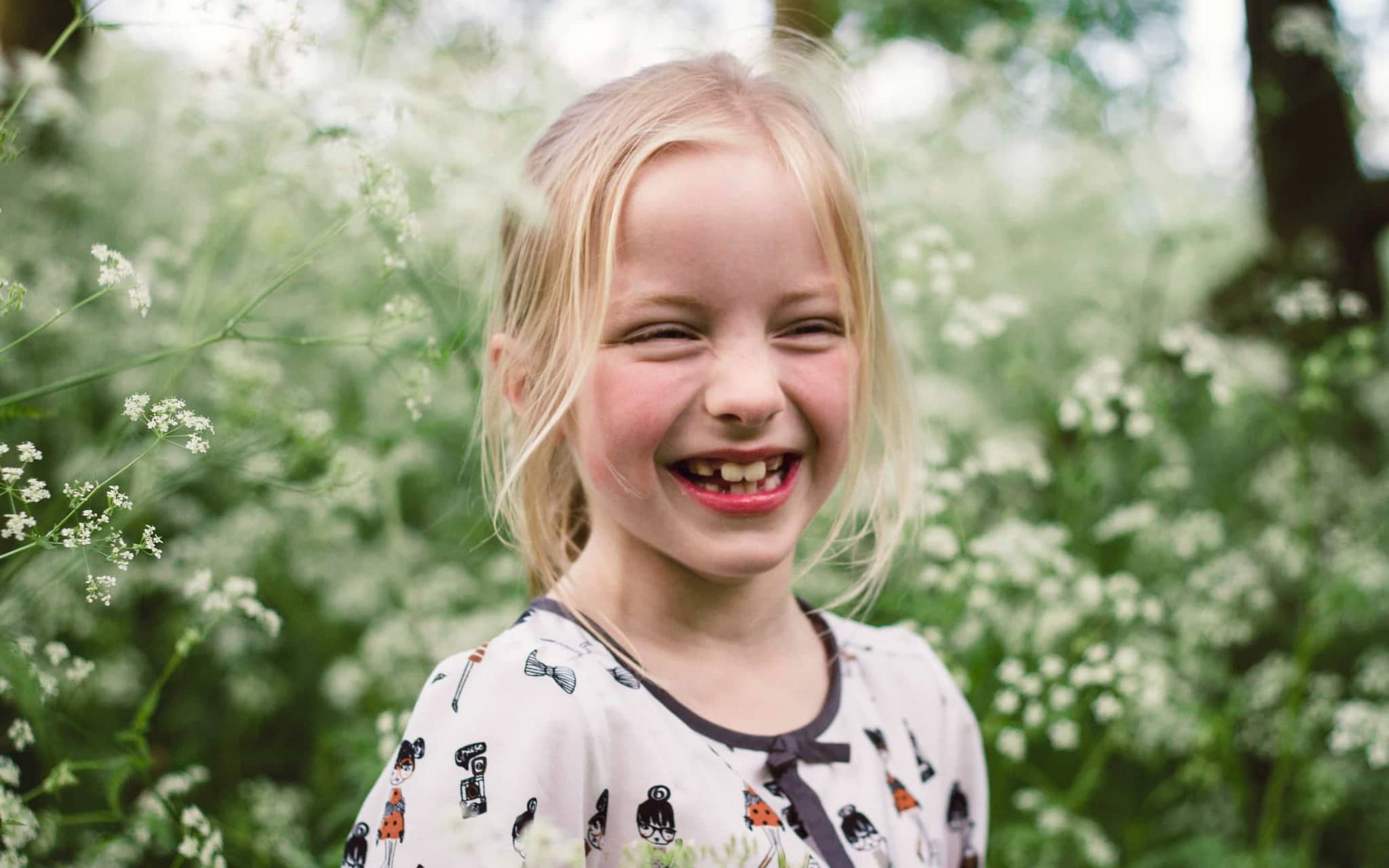 Karies: Mädchen auf einer Wiese lacht mit offenem Mund.